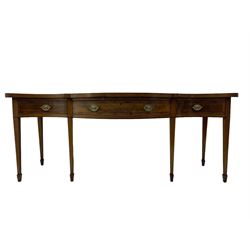 Large George III mahogany serpentine serving table, shaped top with crossing banding and stringing, the frieze fitted with three cock-beaded drawers, oval pressed brass handle plates decorated with urns, on square tapering supports with spade feet 