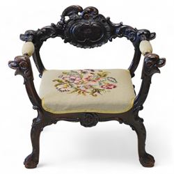 19th century Italian heavily carved stained walnut open armchair, the back rail carved with a large central cartouche decorated with extending acanthus and C-scroll motifs, the wing and arm terminals carved in the form of snarling dog masks, seat upholstered in floral needlework, shaped apron carved with cartouche and shell motifs, over out-splayed cabriole supports with acanthus moulding, terminating to paw feet