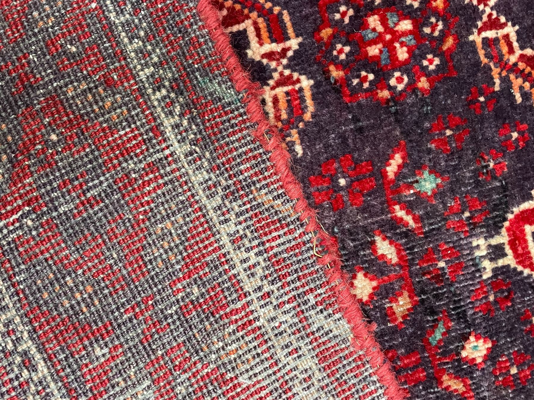 Persian Baluchi dark indigo and crimson ground rug, the field decorated with rows of repeating Pitrak motifs and surrounded by small bird and flower head motifs, floral urn decorated spandrels, repeating Pitrak border within guard stripes