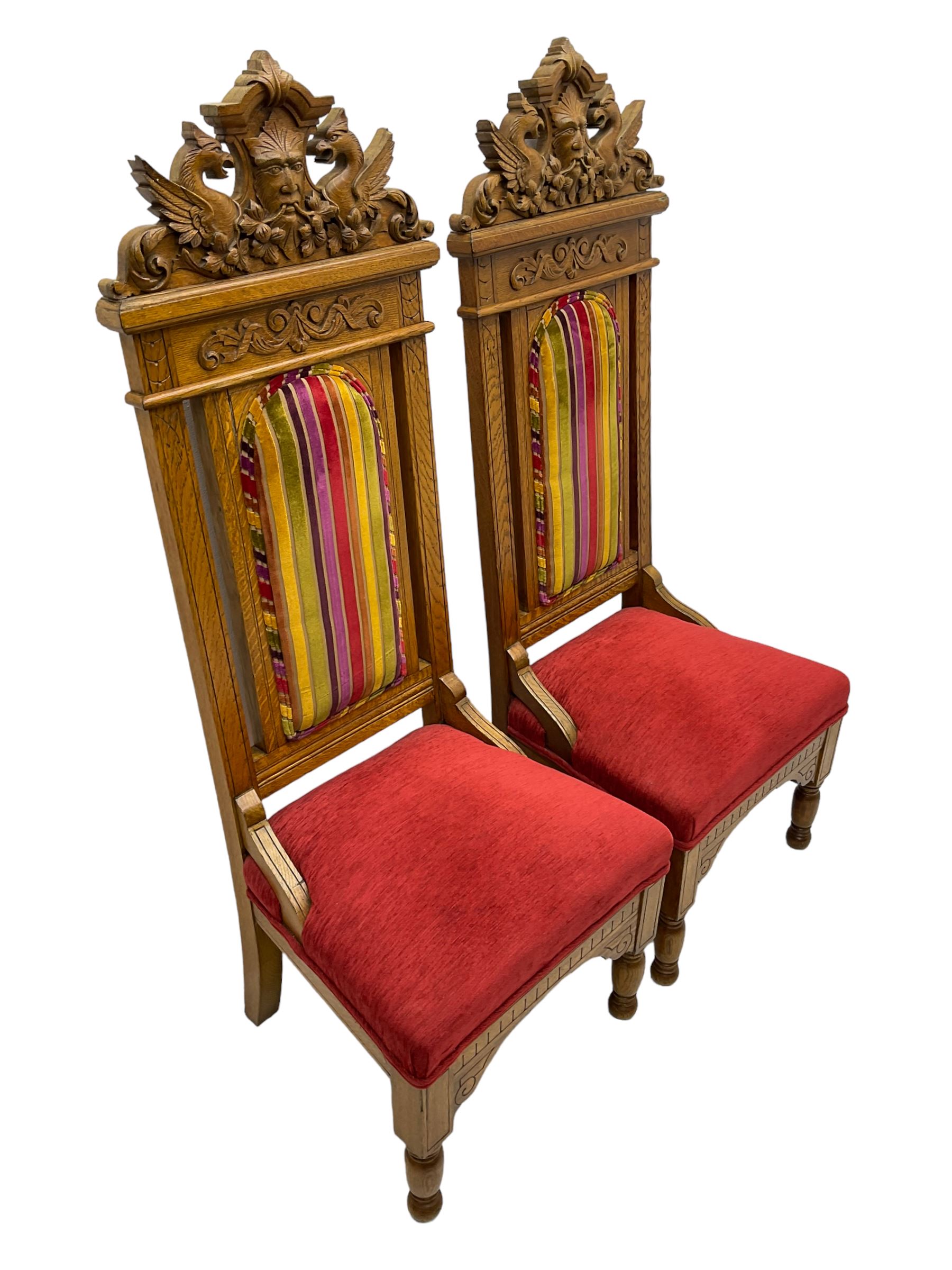 Set of six 20th century Carolean design oak high back chairs, the pediment carved with dragons and central Green Man mask with trailing foliage, the backs upholstered in striped fabric, on turned front supports