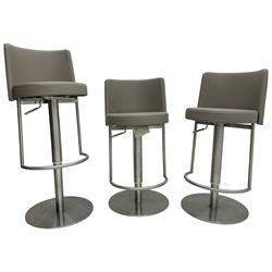 Three contemporary polished metal adjustable Monza bar stools, with taupe faux leather upholstered seats, supported by a brushed stainless steel pedestal base with integrated footrests