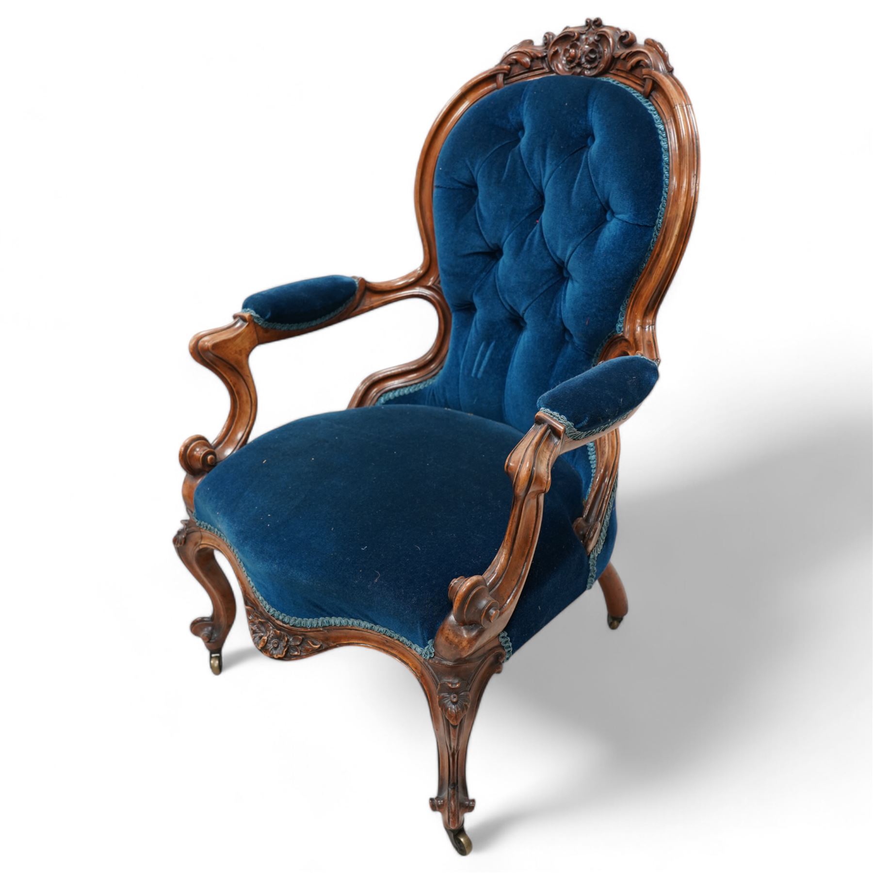 Victorian walnut framed open armchair, curled leaf carved cresting rail over scrolled and shaped arms, upholstered in buttoned blue velvet fabric, on cabriole feet