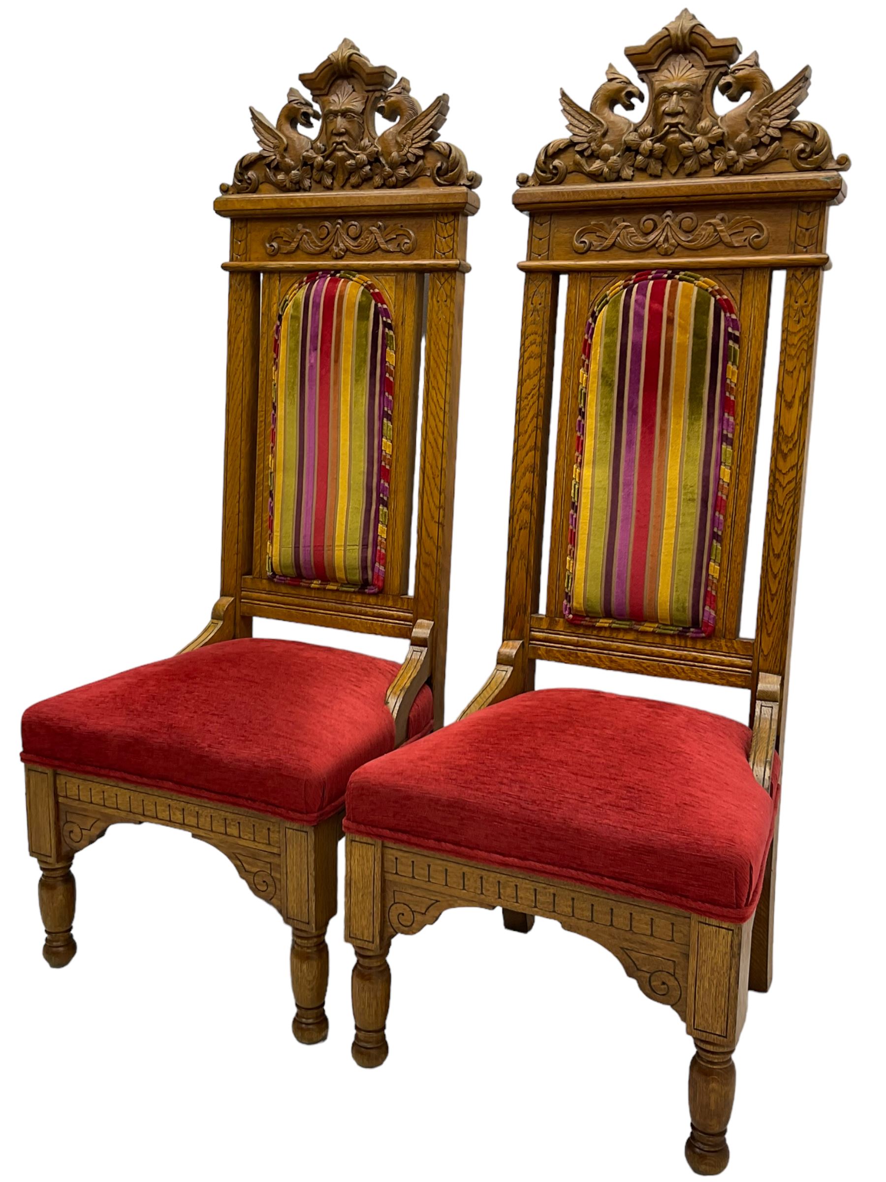 Set of six 20th century Carolean design oak high back chairs, the pediment carved with dragons and central Green Man mask with trailing foliage, the backs upholstered in striped fabric, on turned front supports