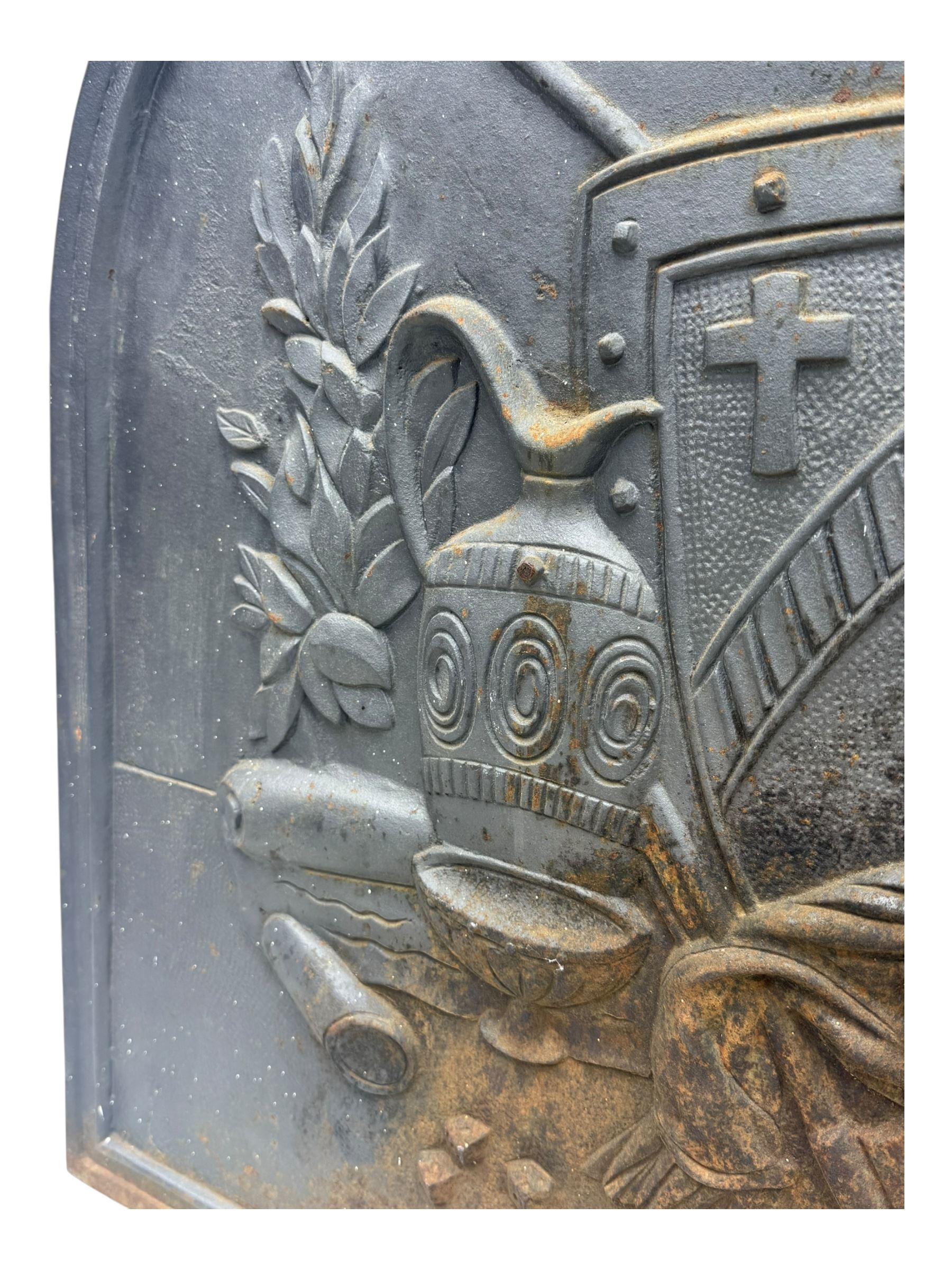 French cast iron fireback, arched form with relief of medieval armour and heraldic symbols, including a shield with a cross and a plumed helmet