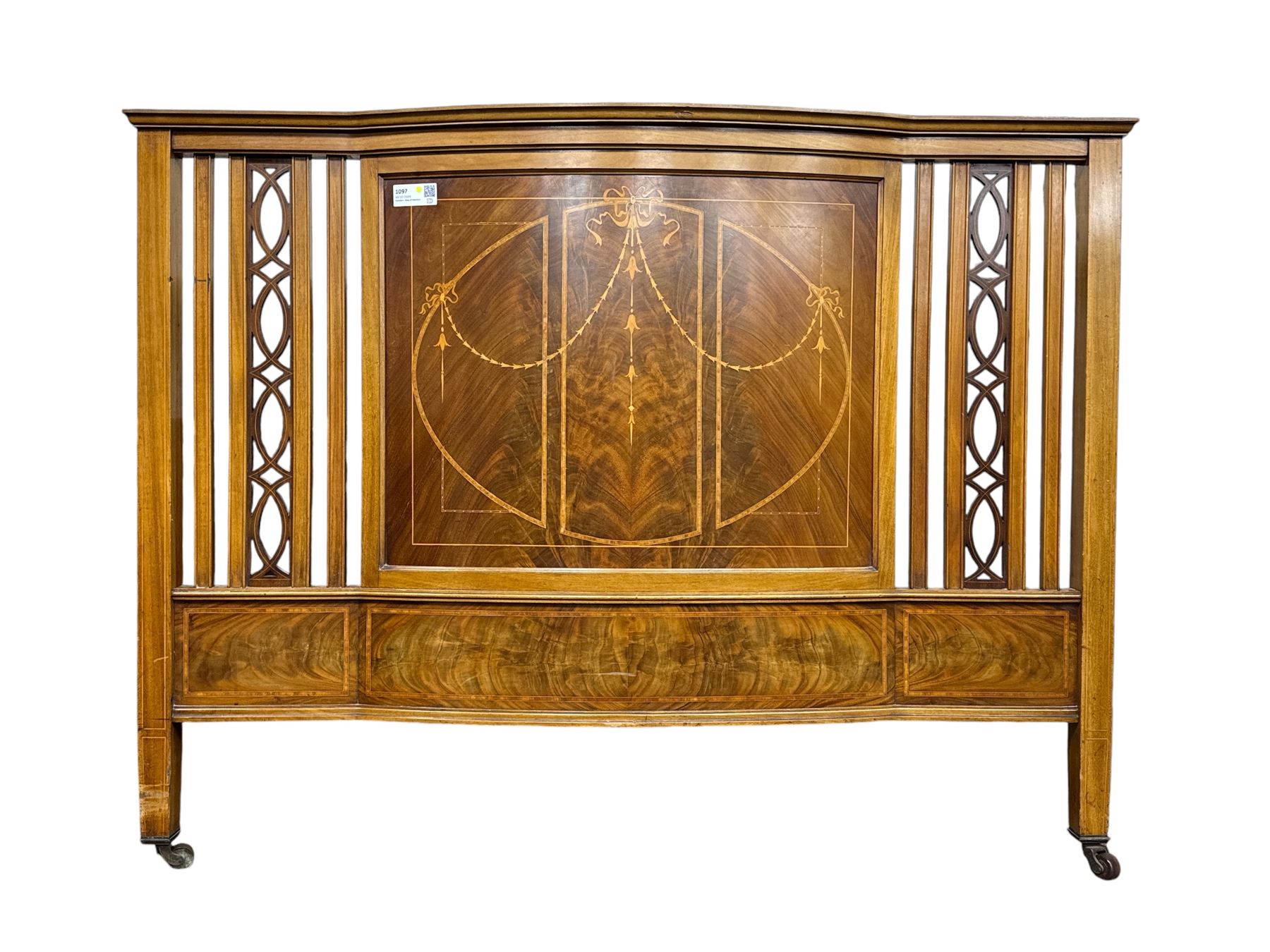 Edwardian mahogany double bedstead, the headboard with central book-matched mahogany panel, decorated with satinwood inlaid swags and ribbons, flanked by openwork carved vertical supports, complete with matching footboard and folding upholstered base