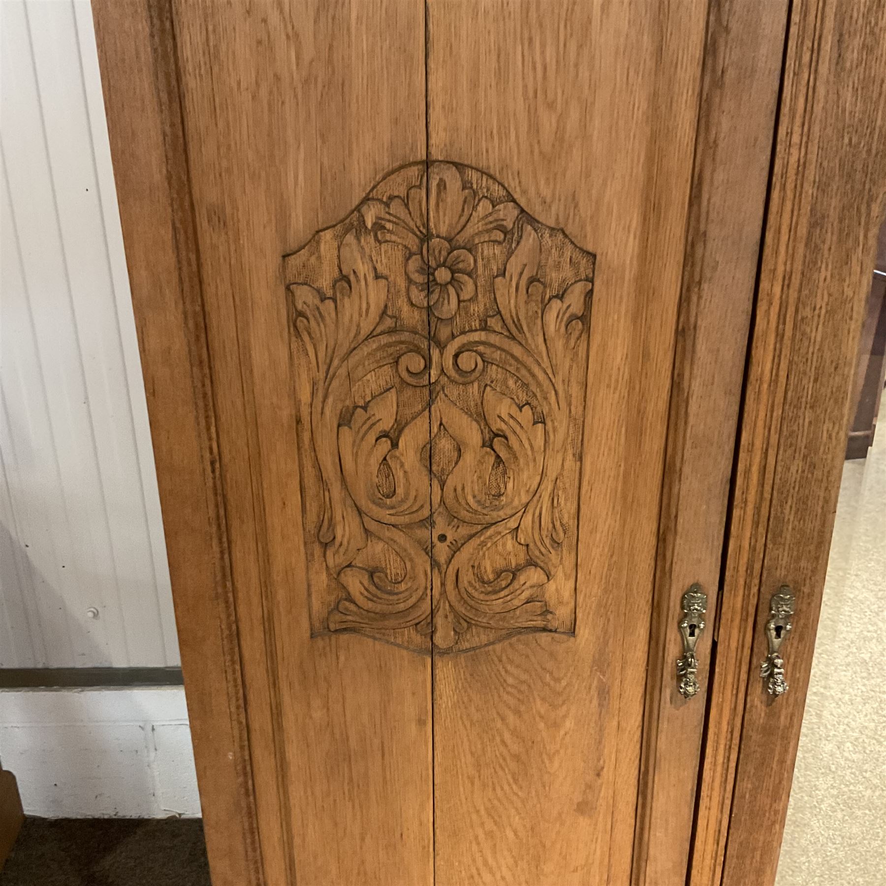 Late 19th century oak triple wardrobe, wide central bevelled mirror door, flanked by two panelled doors each carved with scrolling leaves and flower heads, on moulded skirt base 