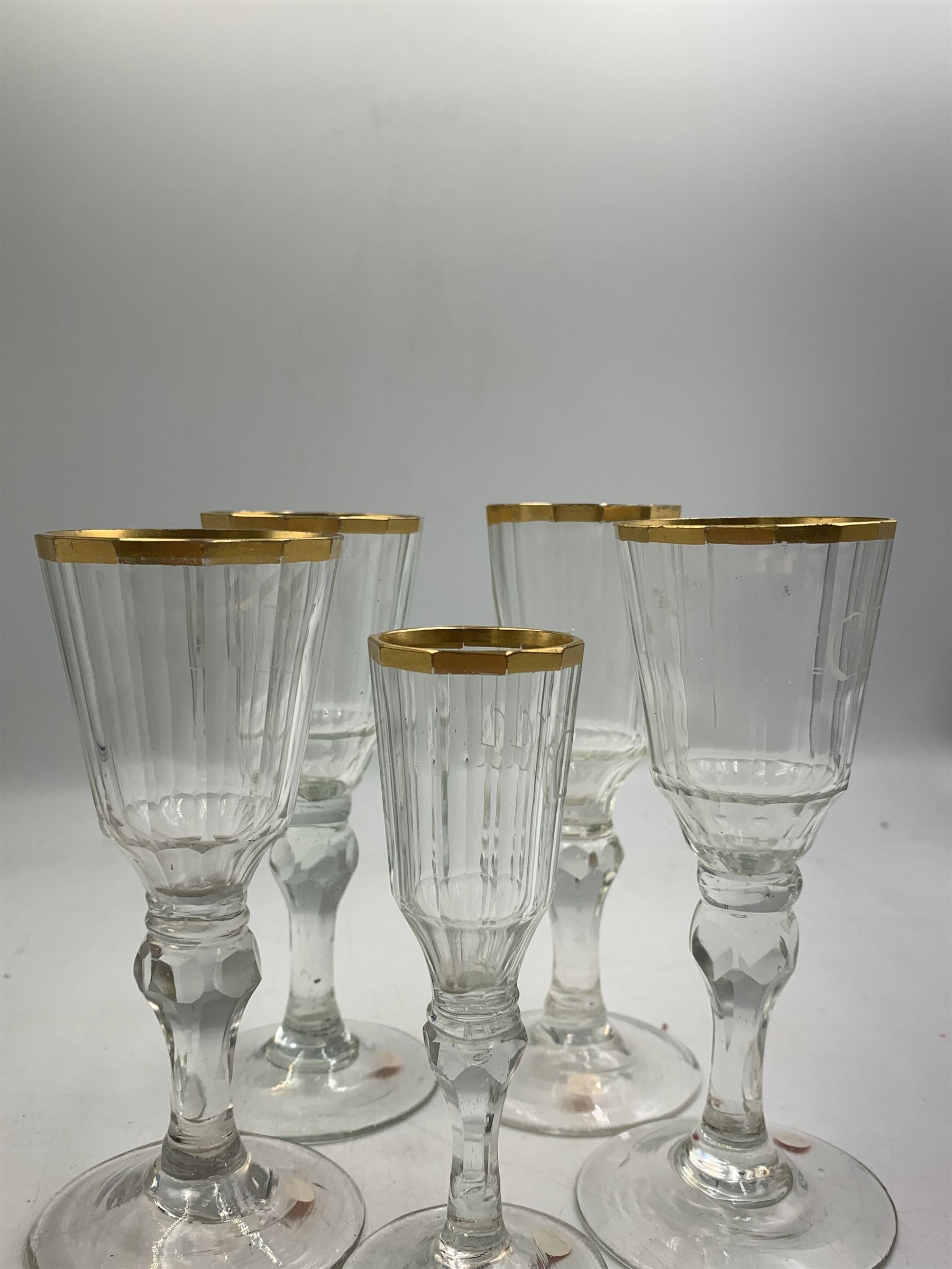 Set of four 19th century Baccarat liqueur/sherry glasses, circa 1820, with panelled bucket bowls and gilt rims, engraved CEG, to faceted knopped stems, together with another smaller example, H14cm and H12cm (5)