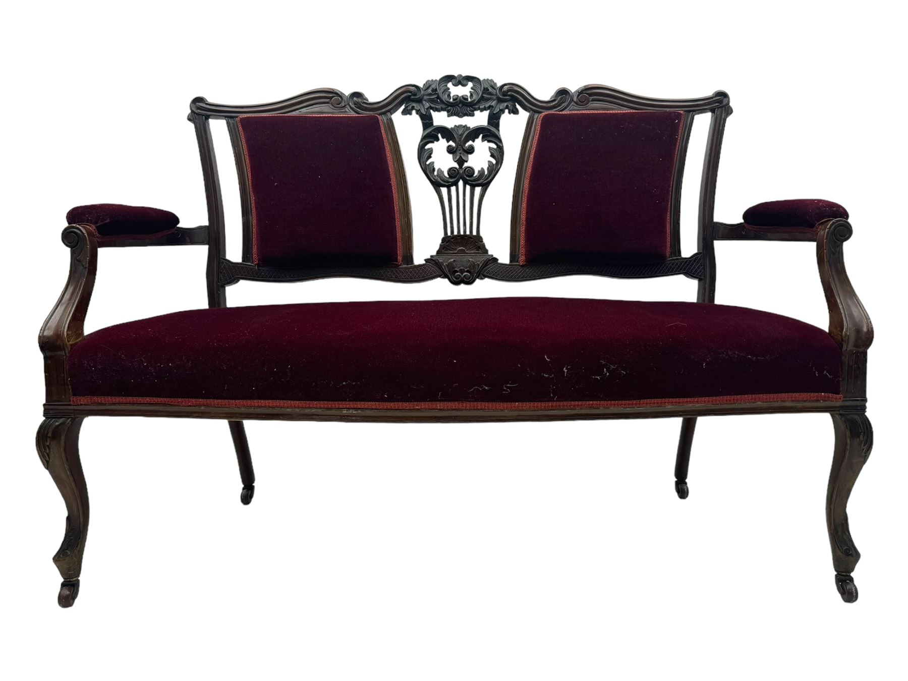 Late Victorian dark oak framed sofa, the backrests, seat and padded arms upholstered in deep red fabric, carved crest rail with scroll and foliate motifs supported by carved uprights, on cabriole supports with leaf carvings terminating in castors