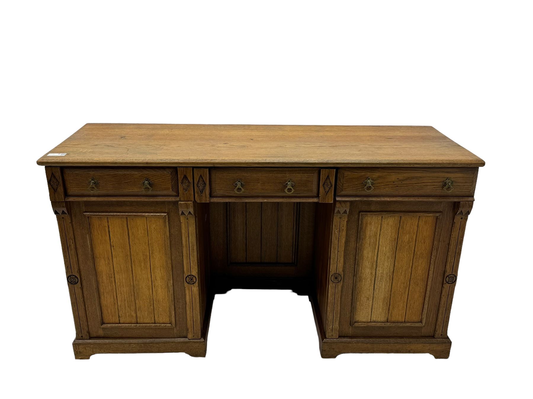 Late Victorian oak twin pedestal desk, chamfered rectangular top over three convex front edge drawers and two panelled cupboards, flanked by carved supports with roundels and diamond motif, on bracketed plinth base