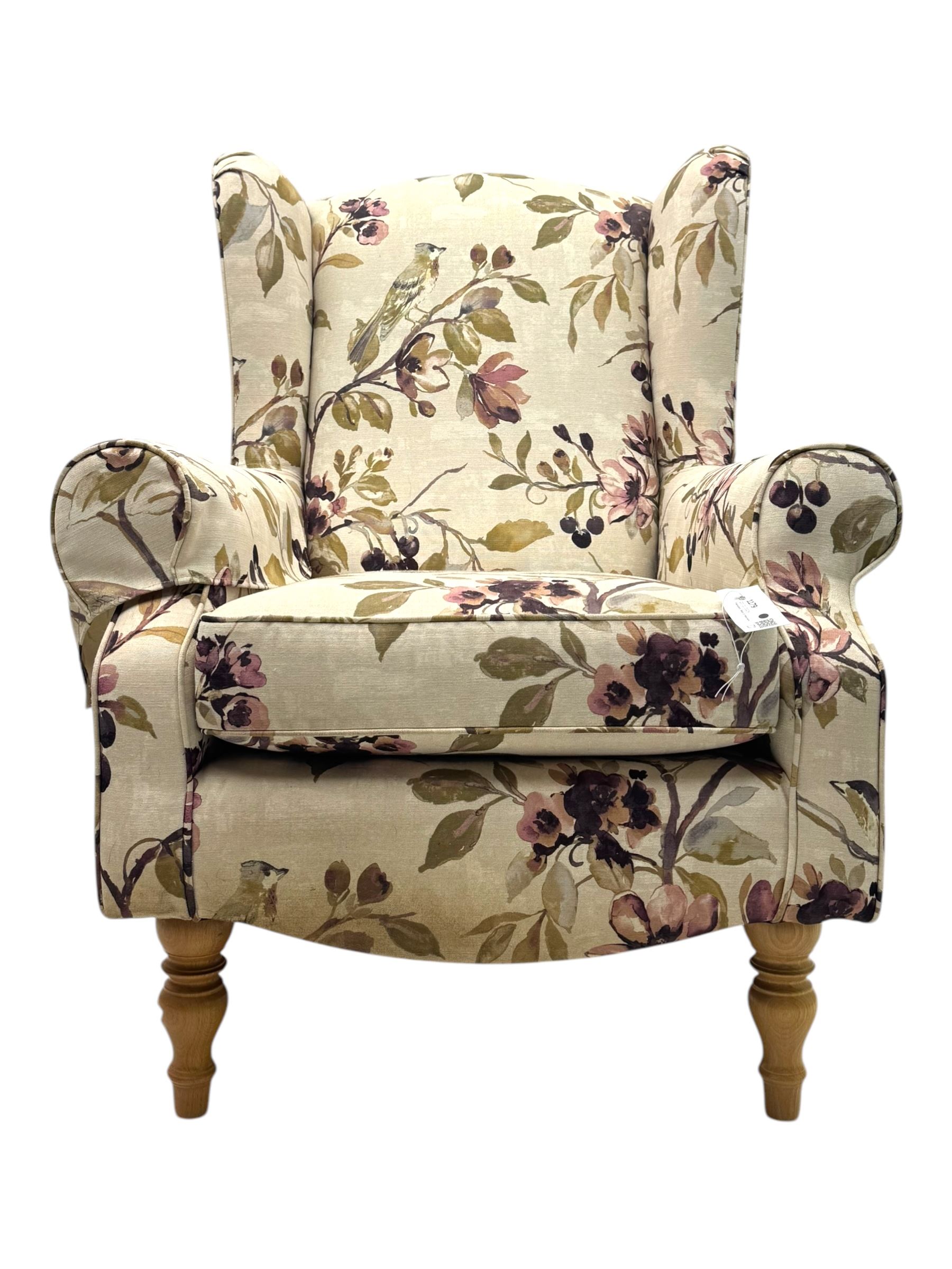 Hardwood-framed wingback armchair, upholstered in cream floral pattern fabric, on turned front feet