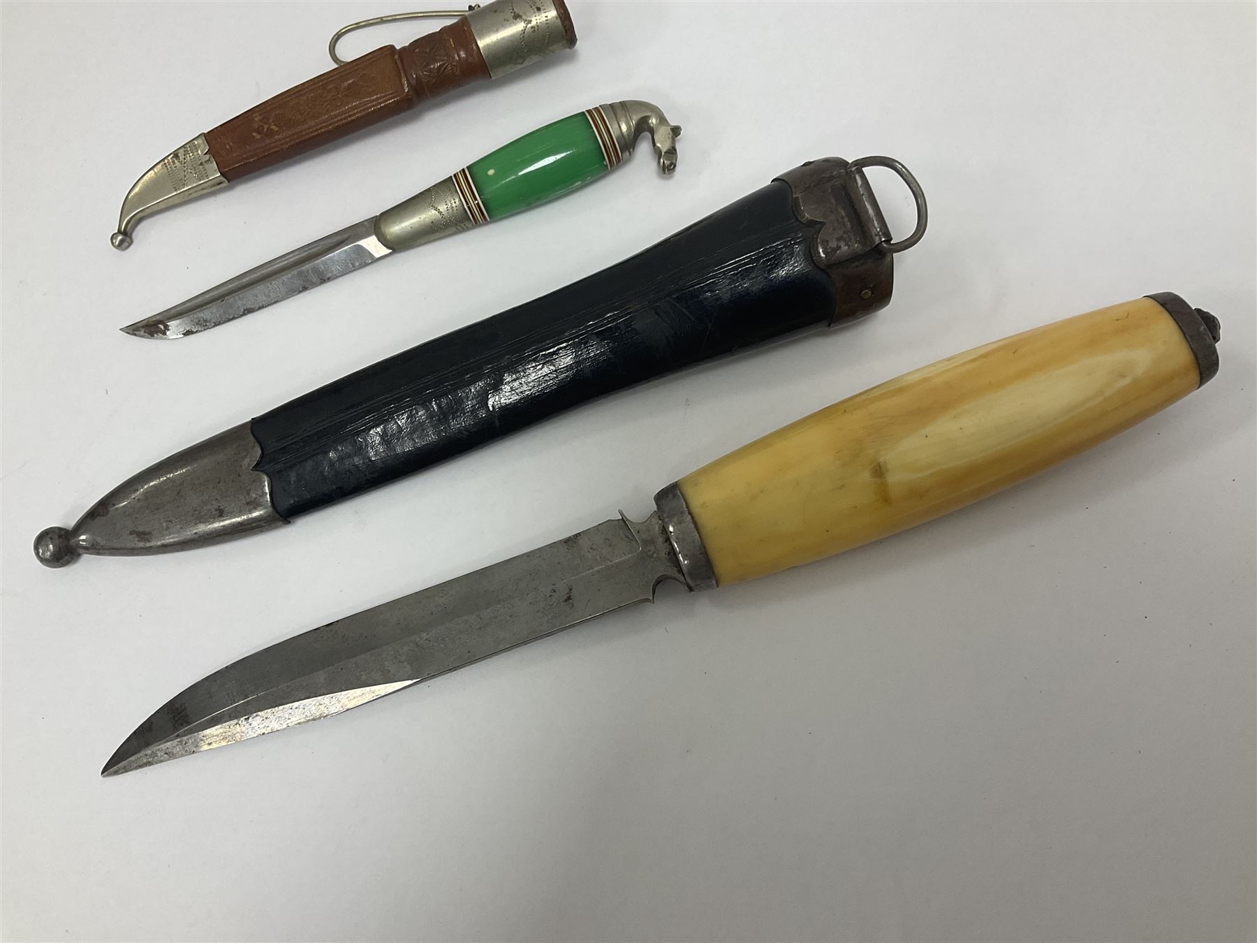 Two Scandinavian bowie knives, the first example with polished green handle with horse head final in white metal, with brown leather sheath, blade L6cm overall L12cm, the second with a polished bone handle, in black sheath with white metal tip, blade L11cm overall 23cm