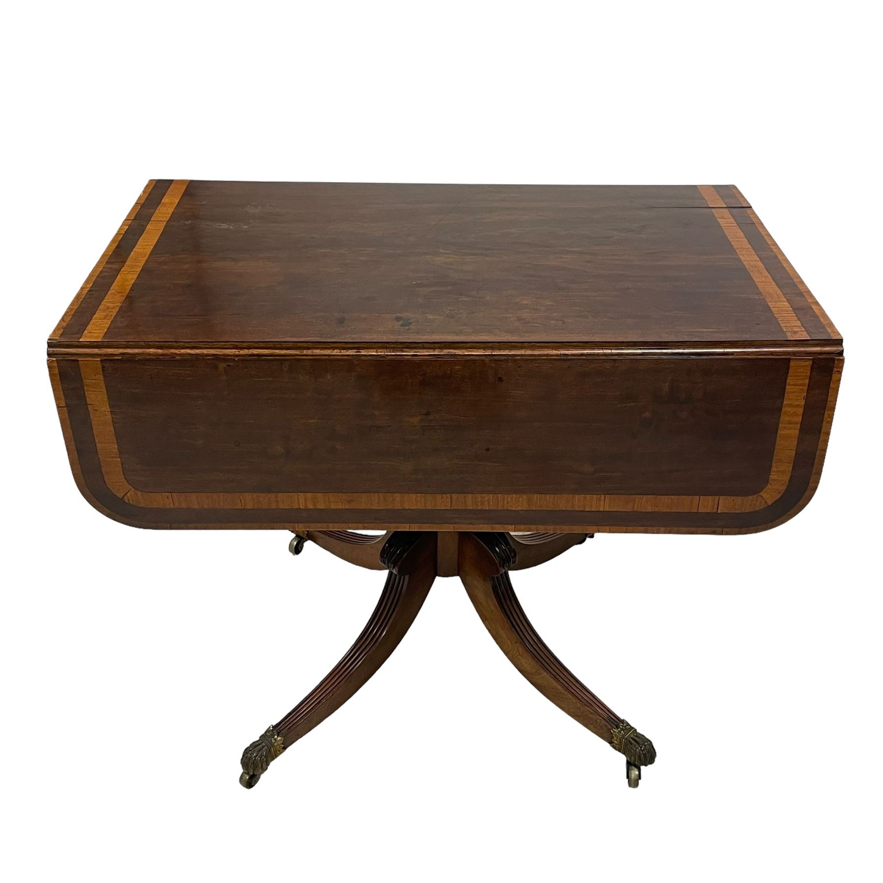 Early 19th century mahogany Pembroke table, rectangular drop-leaf top with rounded corners inlaid satinwood bands, single end drawer and opposing false drawer, turned pedestal on four acanthus carved and reed moulded splayed supports, cast brass cups and castors 