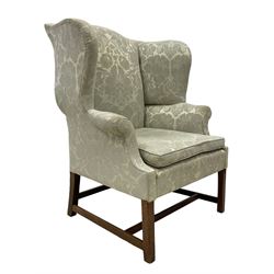 Georgian mahogany framed wingback armchair, upholstered in floral pattern silk damask fabric, wide seat enclosed by rolled arms, on chamfered square supports united by plain stretchers 