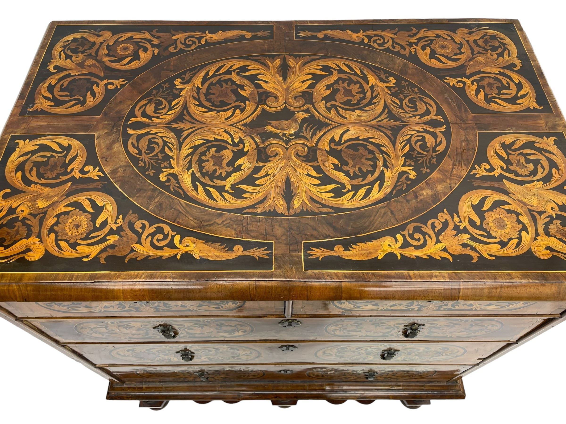 18th century inlaid walnut chest on stand, ovolo-moulded rectangular top inlaid with ebony panels each decorated with scrolling foliage, flower heads and birds, fitted with two short over three long drawers, the drawer fronts decorated with ebony panels enclosing curled leaf inlays, the base fitted with single drawer on turned supports united by waved stretchers, on turned bun feet 