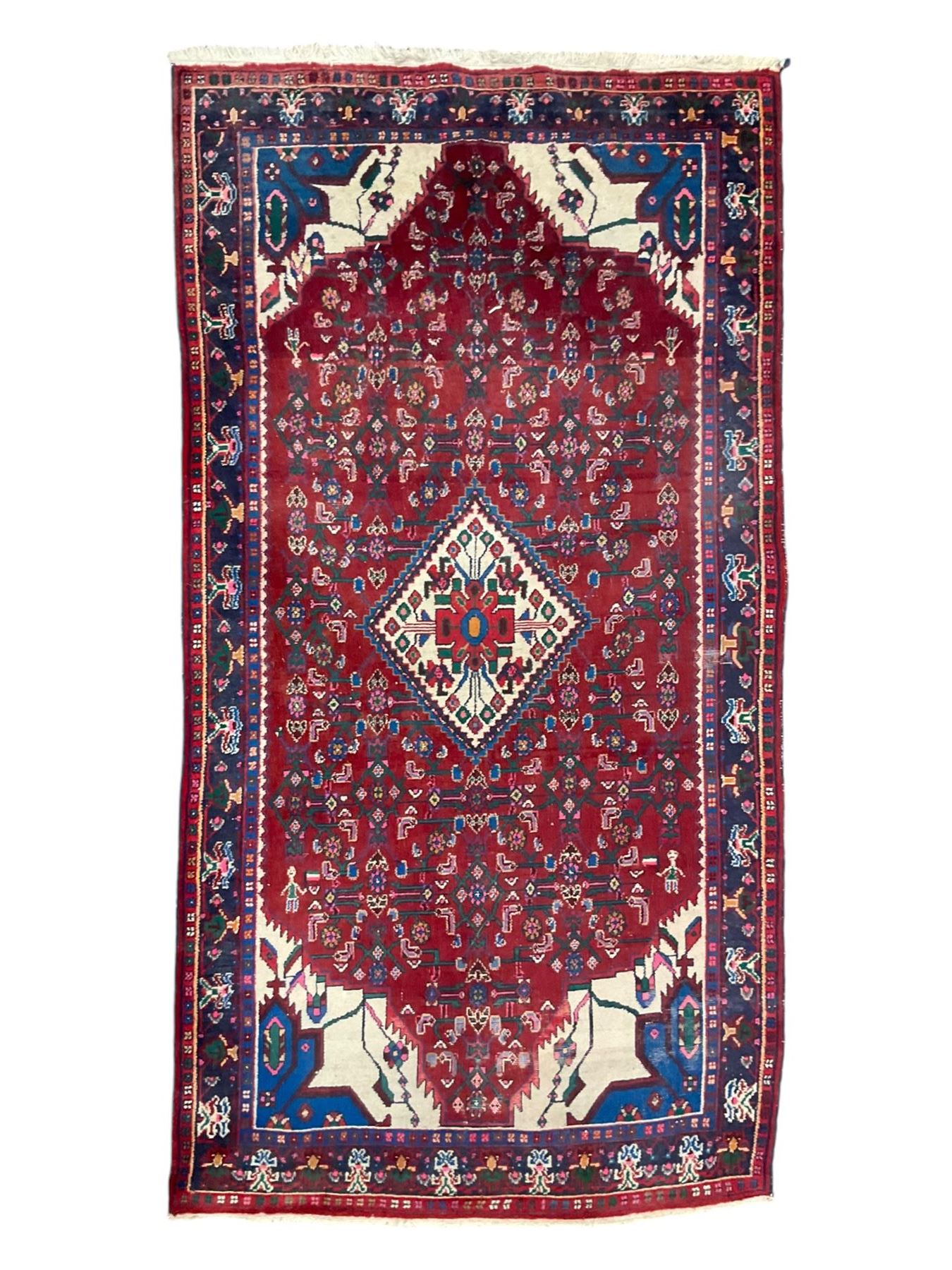 Persian Herati crimson ground rug, the busy field decorated with a central lozenge medallion surrounded by interlocking Herati motifs, the indigo guard band with repeating palmette and stylised plant motifs