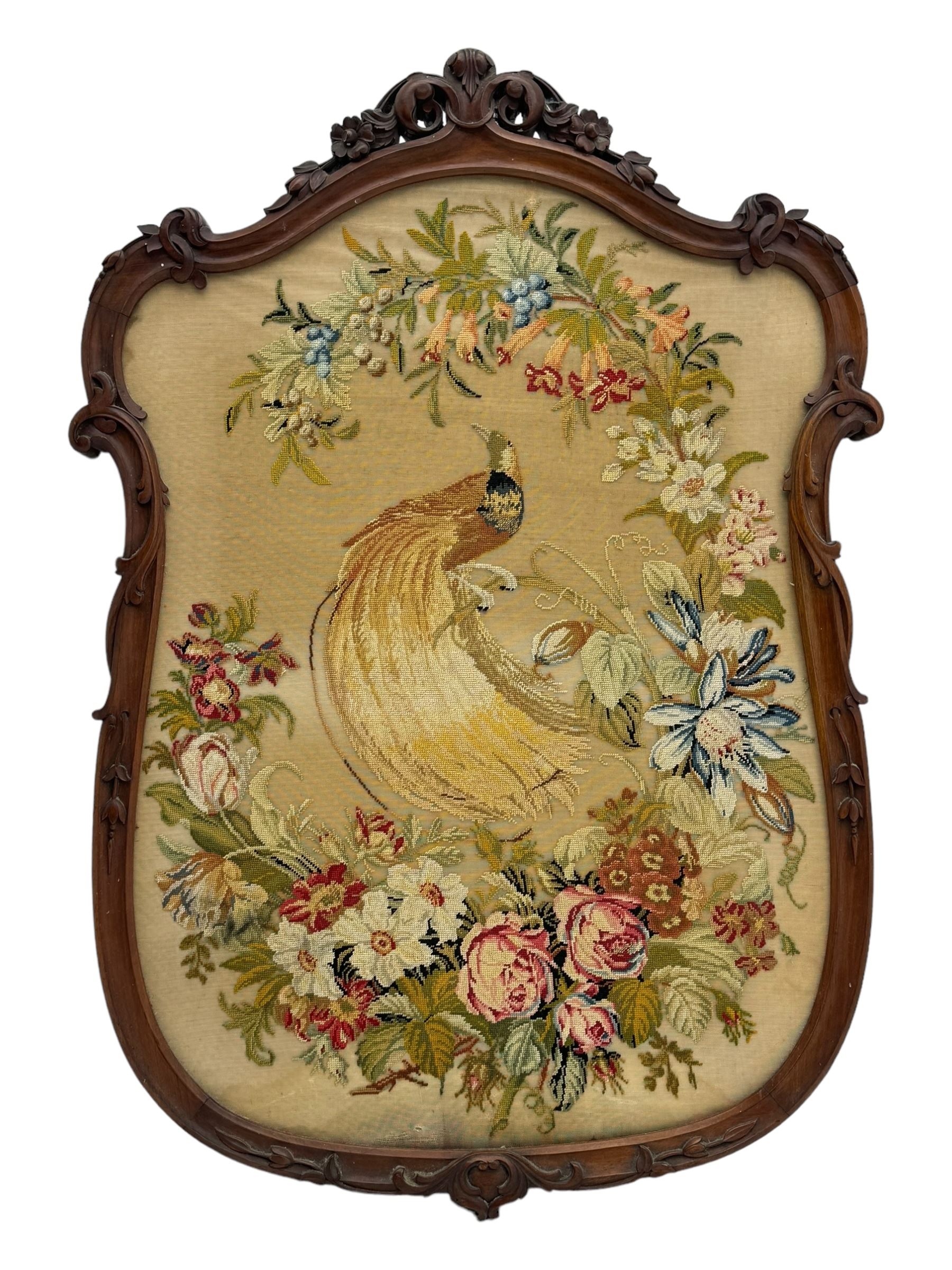 Early 20th century walnut carved needlepoint wall panel, depicting peacock amongst a floral arrangement, framed by carved border with scrolled crest and acanthus leaf accents