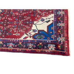 Persian Herati crimson ground rug, the busy field decorated with a central lozenge medallion surrounded by interlocking Herati motifs, the indigo guard band with repeating palmette and stylised plant motifs