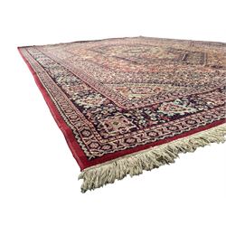 Persian Heriz design red ground carpet, the field decorated with a central star-shaped medallion surrounded by geometric floral motifs and angular vine patterns, the spandrels highlighted with palmette designs, the main border featuring a series of stylised rosettes and leaves against a dark blue ground, enclosed by multiple guard stripes with alternating floral and geometric motifs