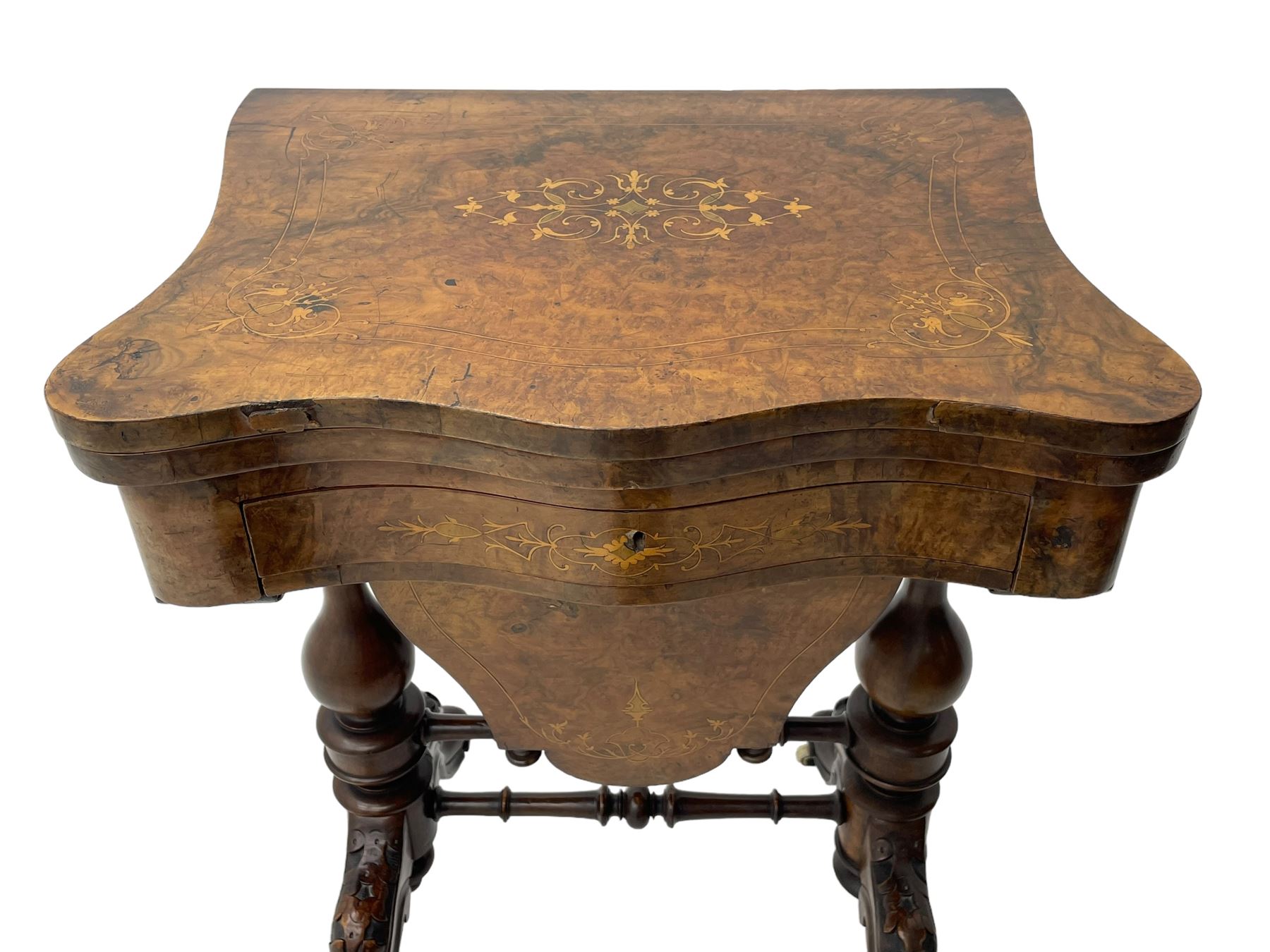 Victorian inlaid figured walnut games table, the serpentine fold-over top inlaid with scrolling foliate decoration, the top opens to reveal cribbage, backgammon and chess boards, single drawer over sliding storage well, on twin pillar supports united by double turned stretchers, on foliage carved out-splayed supports with brass and ceramic castors 