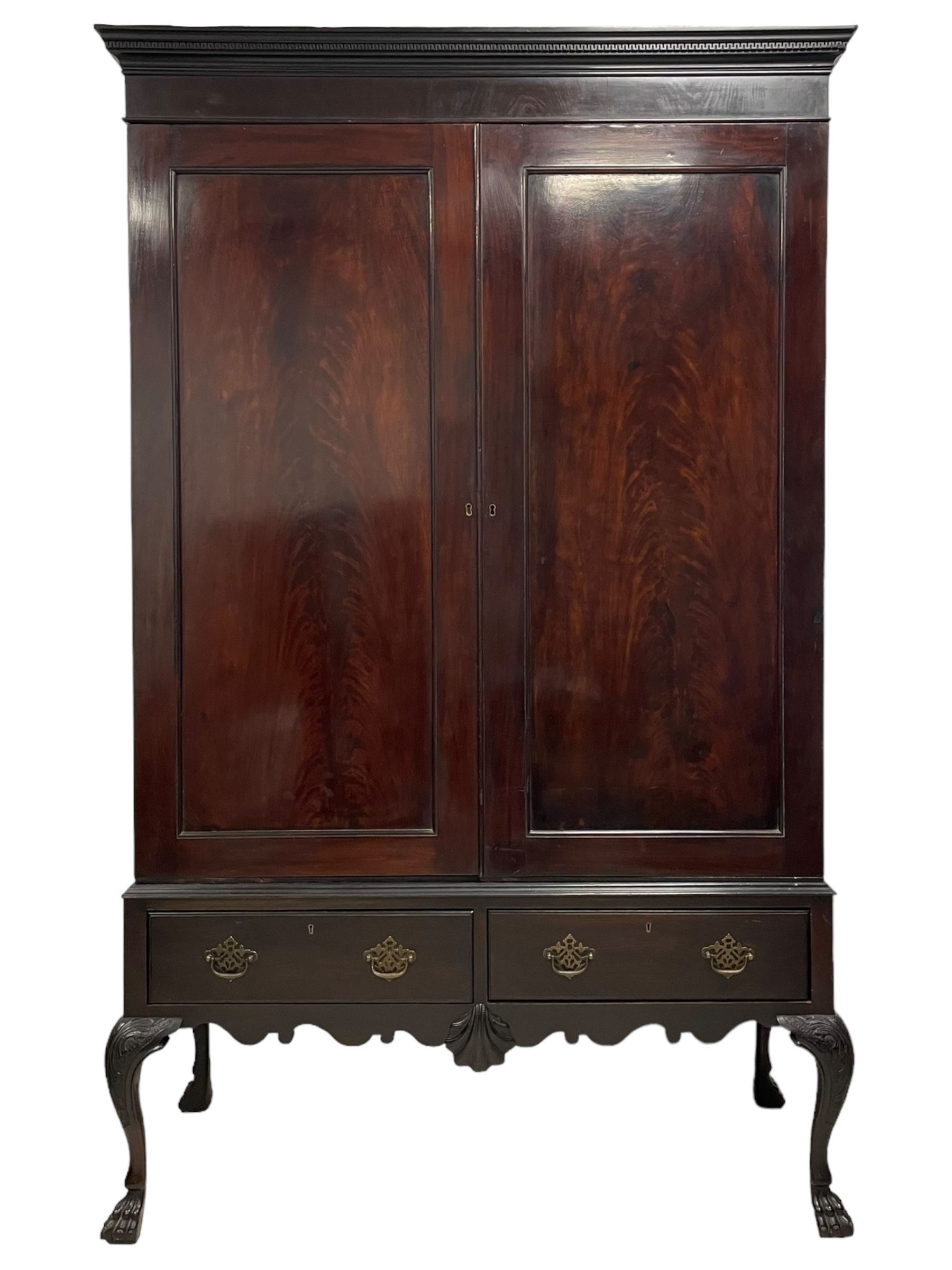 19th century Irish mahogany press wardrobe, projecting dentil cornice over two figured panelled doors, enclosing three sliding trays and hanging rail with coat hooks, fitted with two drawers to base over a shaped apron, raised on acanthus carved cabriole supports with paw feet, retailed by Millar & Beatty of Dublin, with paper labels verso, collected and restored by Michael Butler (1870-1900), impressed stamp to side and ink stamp to drawer inscribed 'M Butler collector of high-class furniture and works of art'