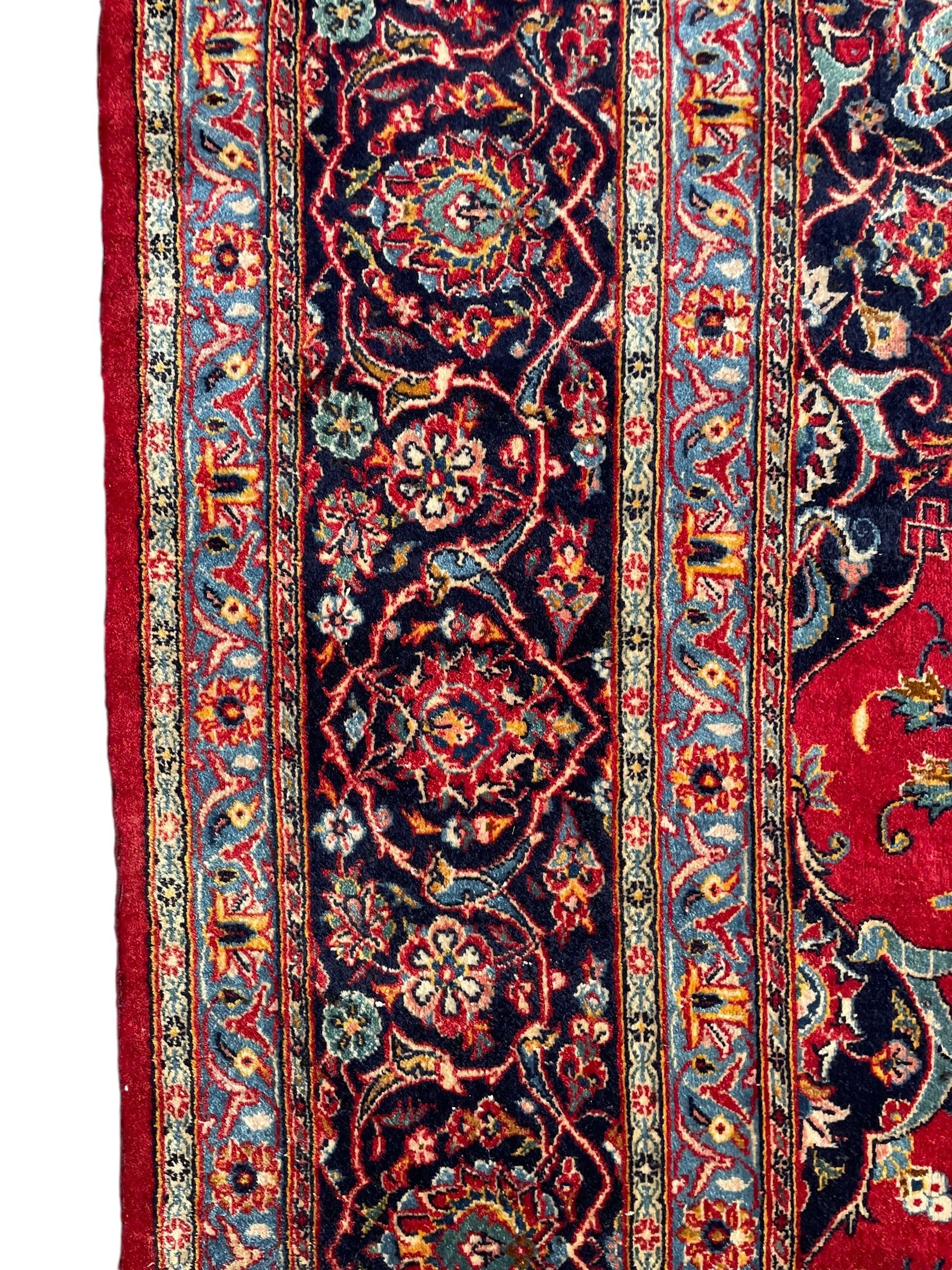 Persian Kashan crimson ground carpet, central rosette medallion on a field of trailing foliate branches decorated with palmettes, scrolling border with repeating plant motifs and flower heads, enclosed within floral pattern guard stripes