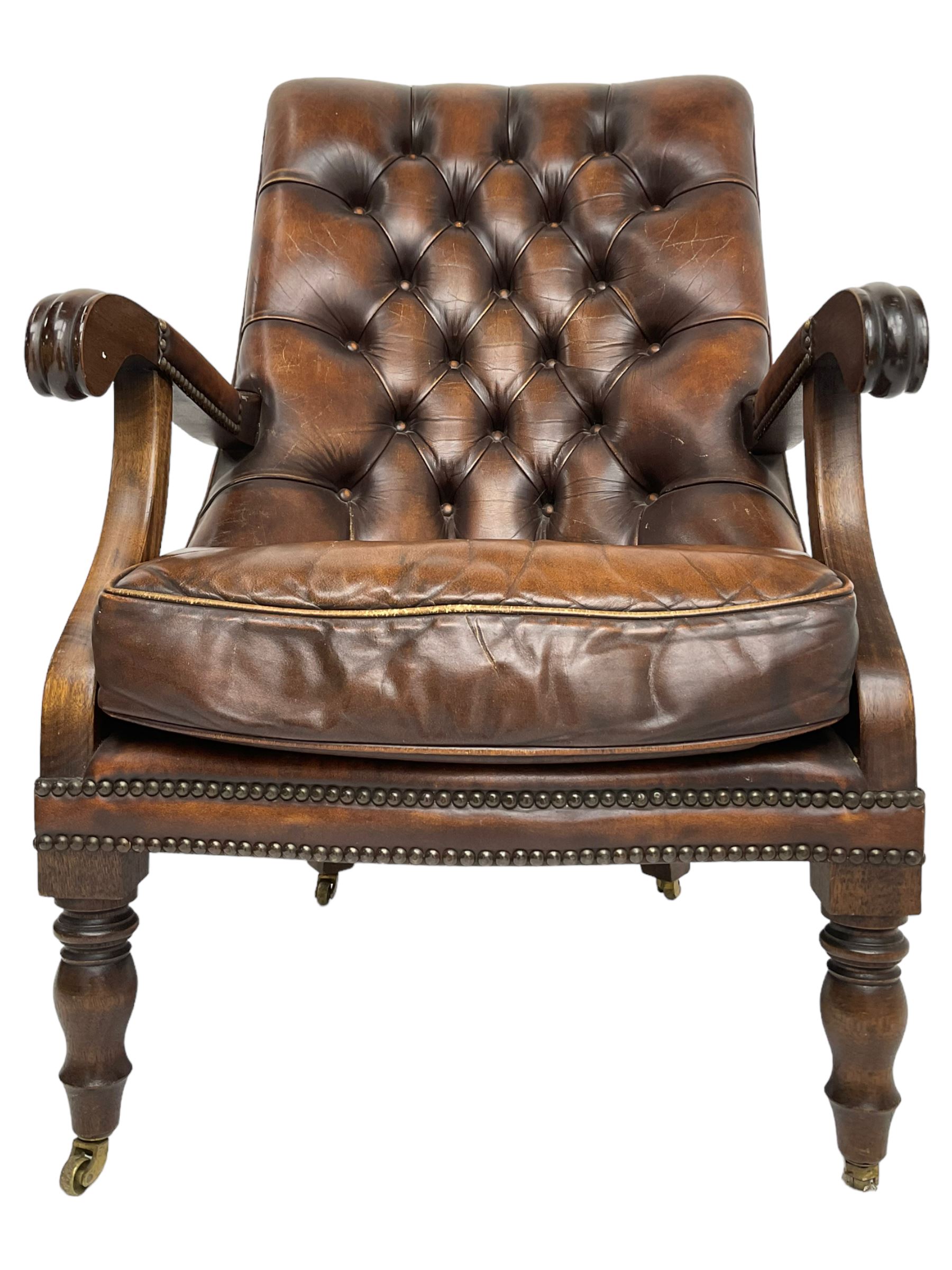 Georgian design mahogany framed library armchair, upholstered in buttoned chocolate brown leather with studwork and loose seat cushion, raised on turned supports with brass castors