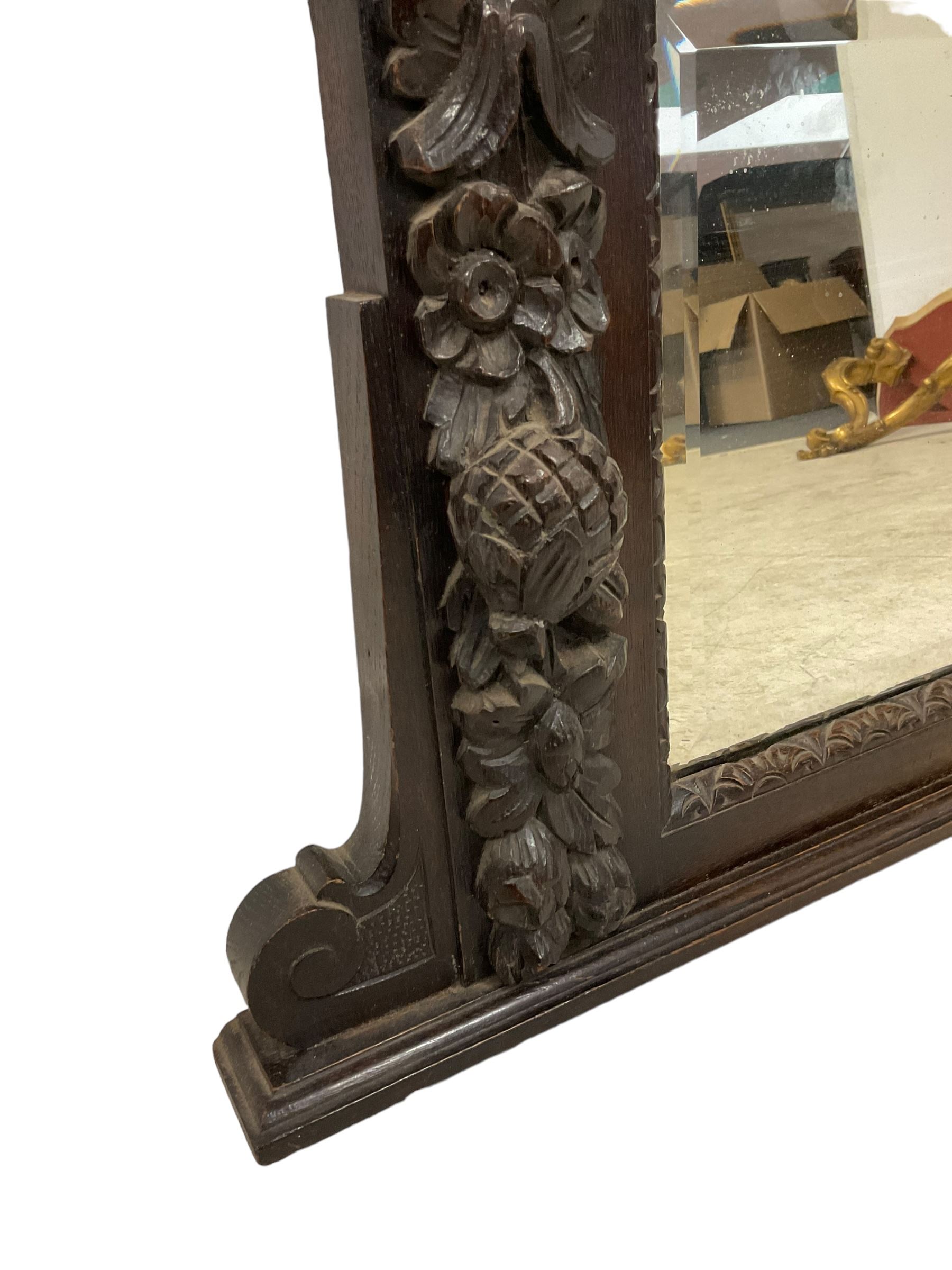 Victorian heavily carved oak wall mirror, projecting gadroon carved ovolo cornice, bevelled mirror plate within a lunette carved frame, decorated with applied fruit and foliage carved mounts, scroll carved brackets 