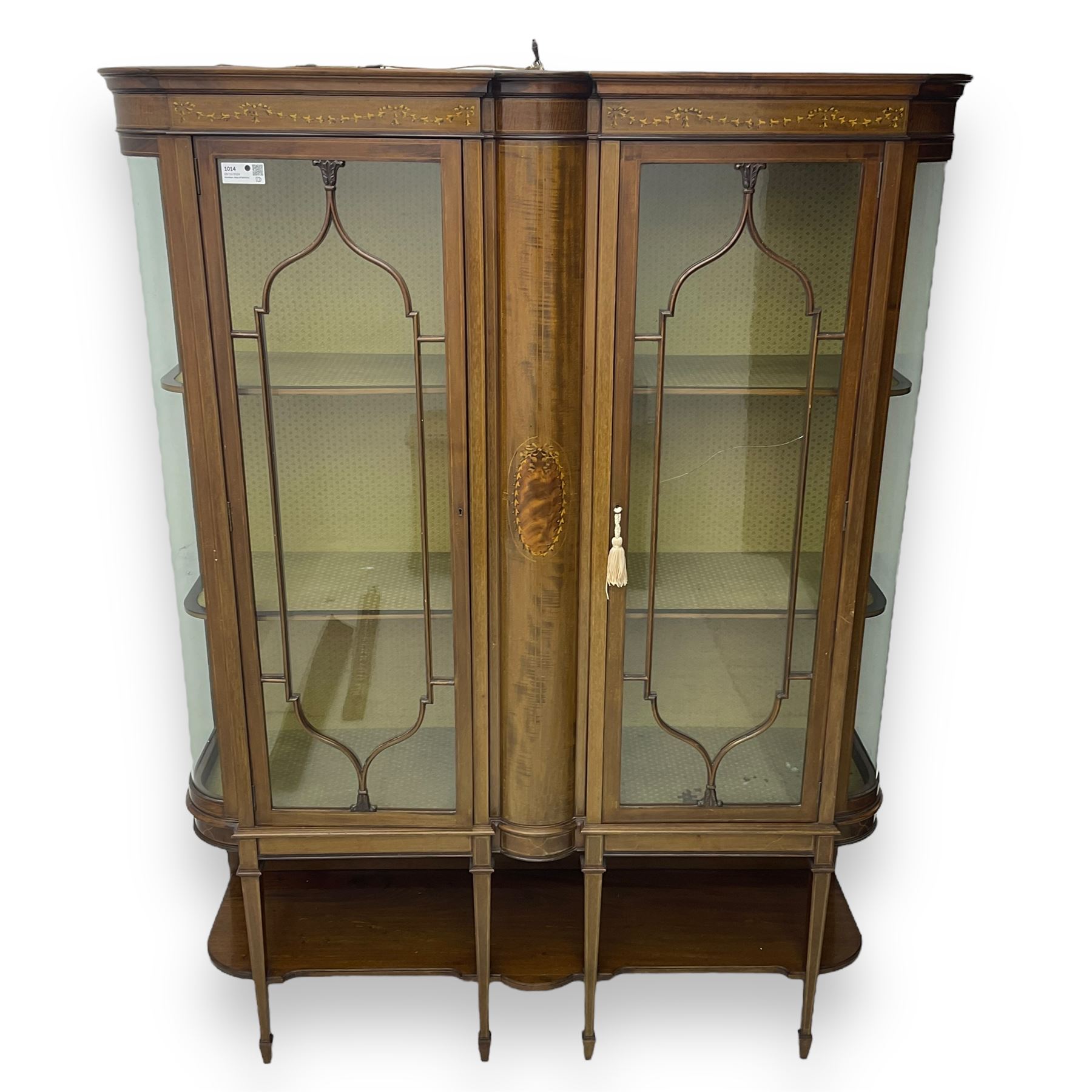 Edwardian inlaid mahogany display cabinet, projecting moulded cornice over two glazed doors, flanked by curved glazed sides and central arched panel with floral medallion, raised on square tapering supports with spade feet united by undertier