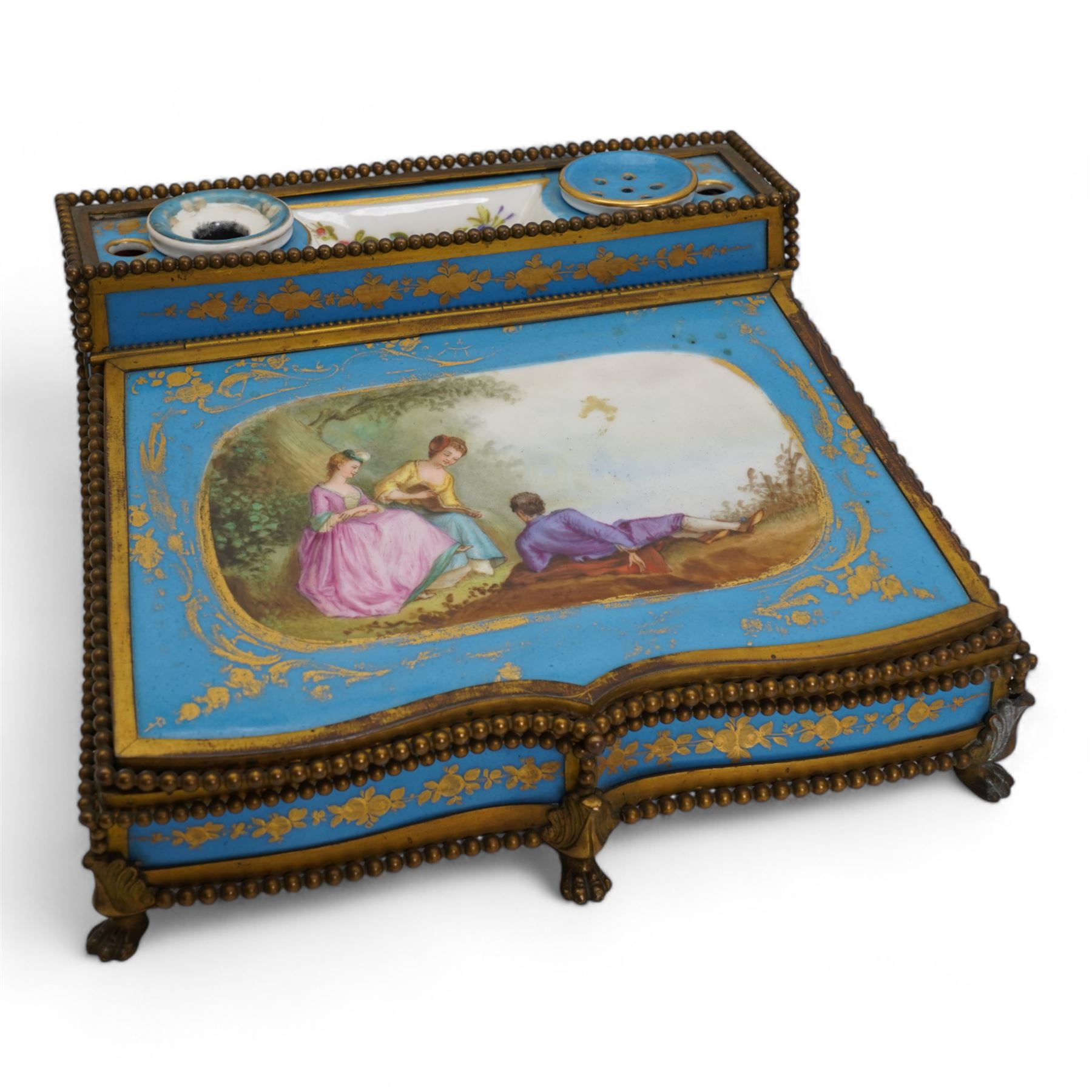 19th century French Sevres style porcelain and gilt brass table top writing box, the fall front painted with three figures in a woodland landscape, within a gilt border on a bleu celeste ground, the side panels depicting floral sprays, the top with removable porcelain inkwell and pounce pot, beaded gilt metal border with four lion paw supports and pink velvet fitted interior, L28cm x H14cm