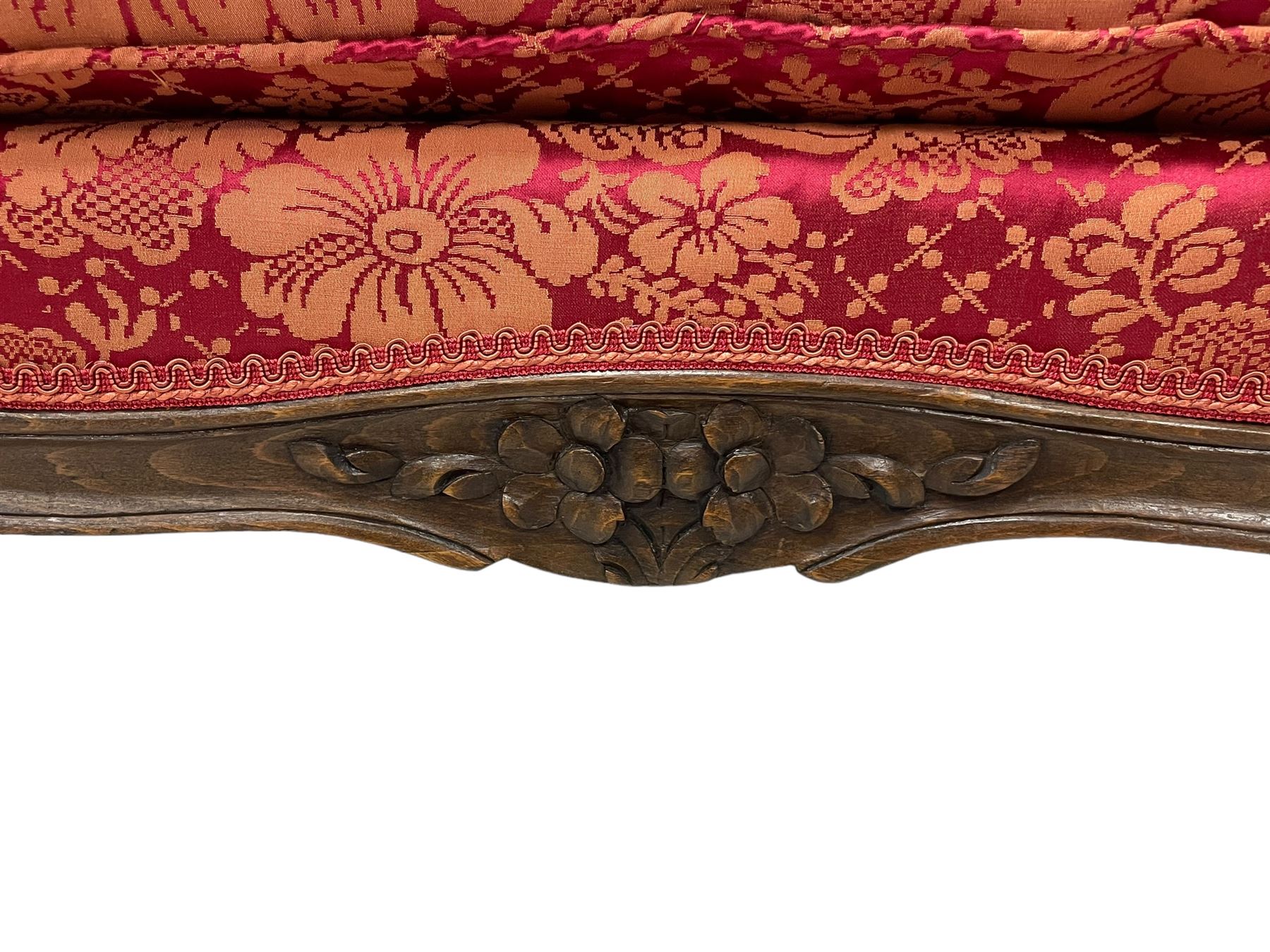 Late 20th century French design stained beech framed armchair and matching stool - the armchair with shaped and moulded frame carved with flower heads and foliage, upholstered in silk red and gold ground fabric with floral pattern, on scroll carved cabriole feet decorated with flower head carvings (W73cm, H82cm, D75cm); the footstool of concaved rectangular form with moulded frame carved with flower heads, upholstered loose cushion, on cabriole feet (70cm x 64cm, H48cm)