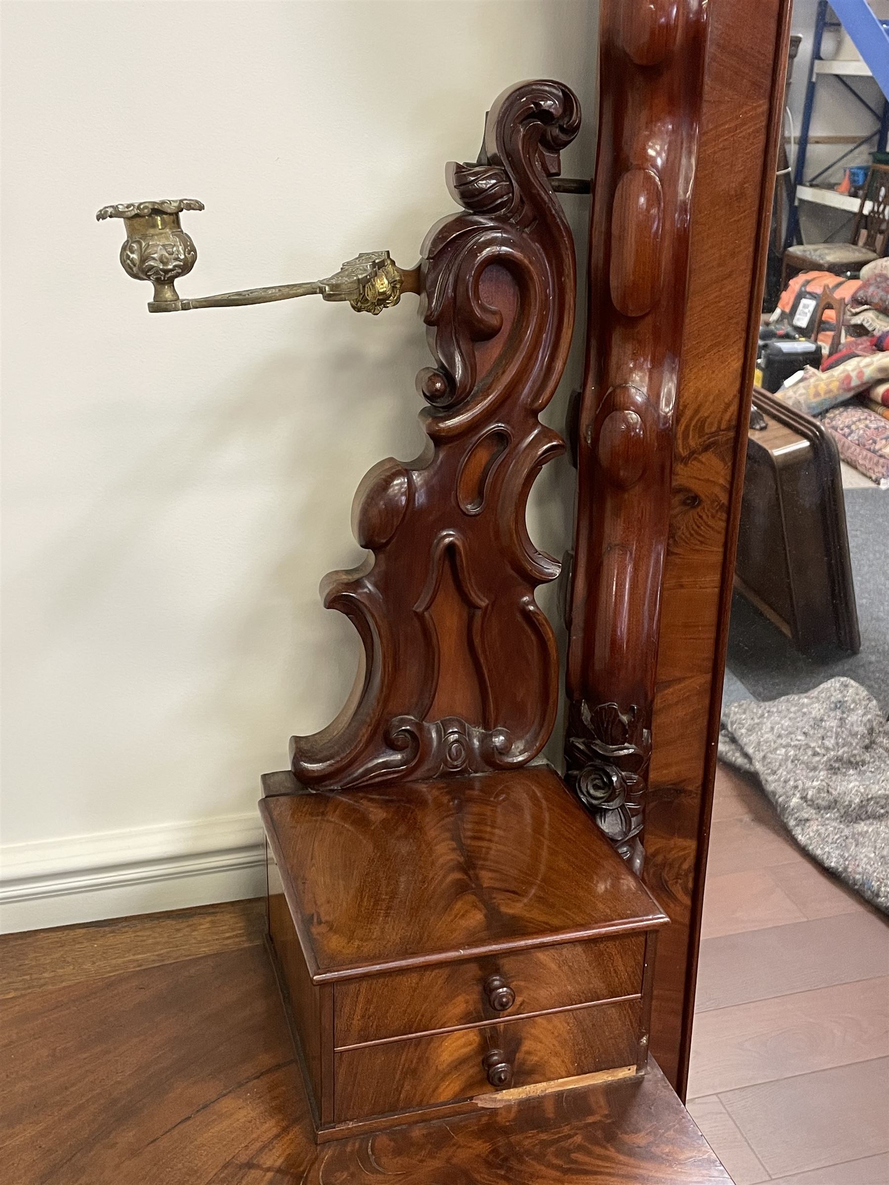 Tall Victorian figured mahogany twin pedestal dressing table, the tall mirror with flower head and scrolled leaf carved pediment, flanked by two turned and carved finials over faceted lancet arched lantern tops, plane mirror plate enclosed by shaped frame, pierced and undulating moulded uprights, on C-scroll and curled leaf carved supports fitted with cast brass hinged candle sconces, each pedestal fitted with two small trinket drawers over larger drawer and panelled cupboard, canted corners with matched upright mounts, the cupboard doors enclosing slides, on scroll carved feet 