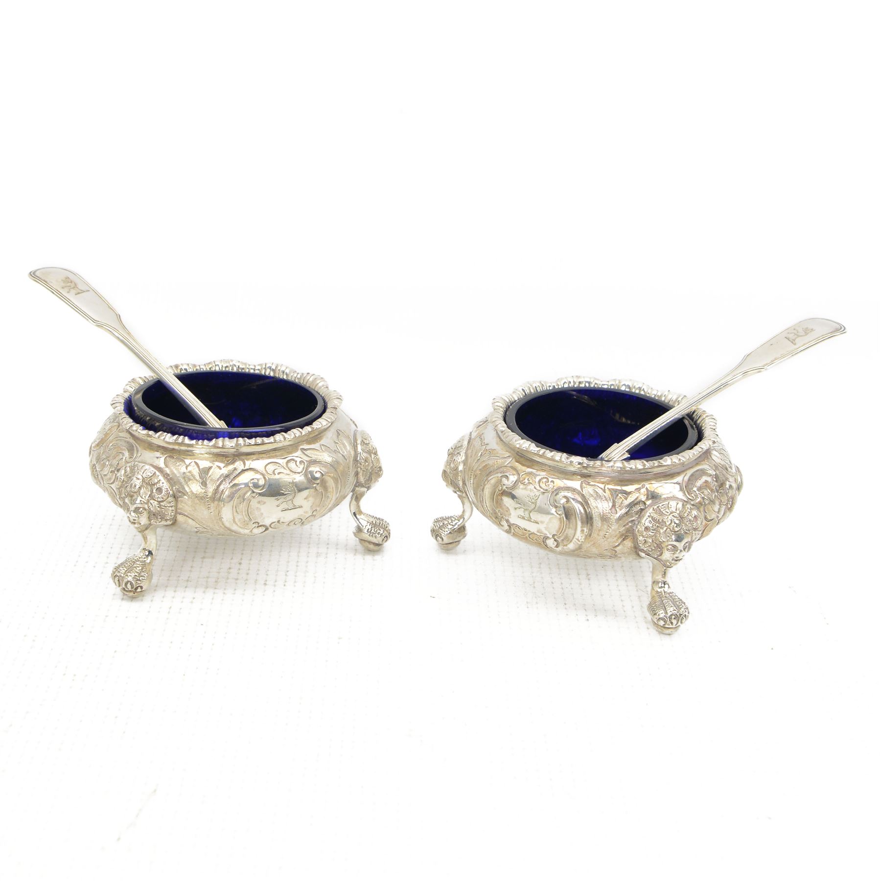 Pair of Victorian silver circular salts with blue glass liners, embossed floral decoration and claw and ball feet London 1855 Maker William Robert Smily and a pair of George IV silver salt spoons with gilded shell bowls