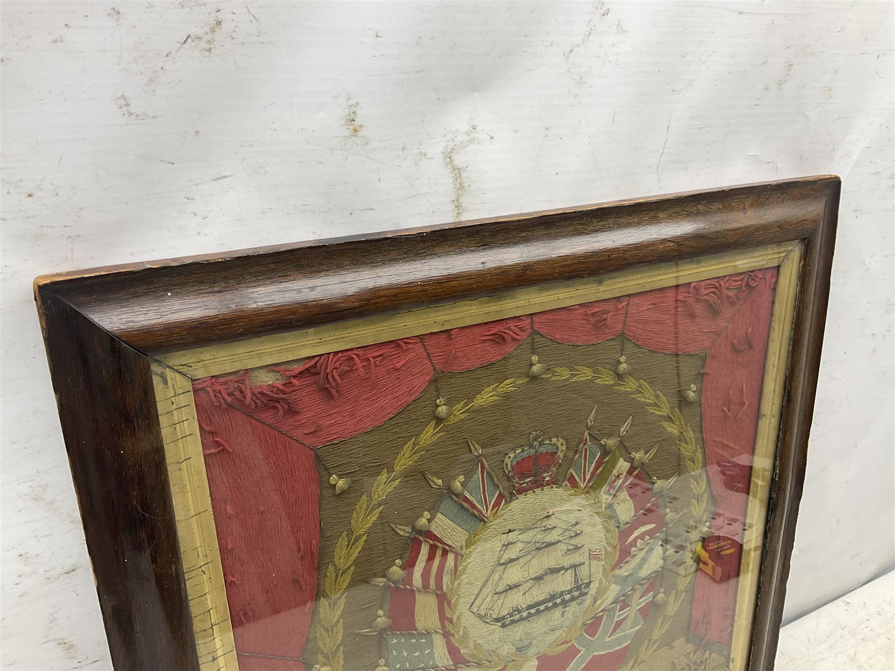 19th century woolwork, depicting a clipper ship, fully rigged over black hull with white ports, within a border of ensigns and flags and beaded crown above, in glazed wooden frame, H57cm