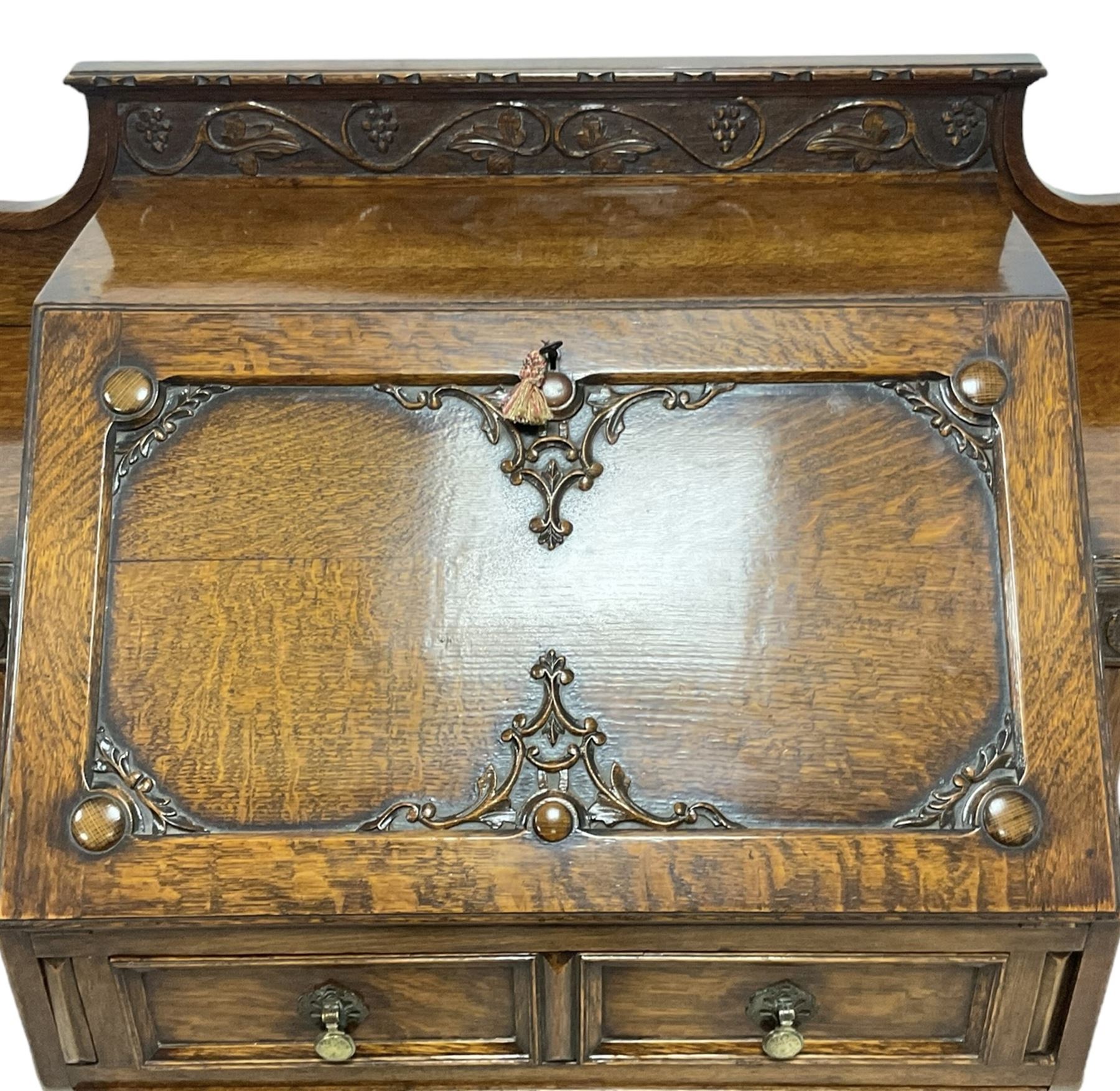 Early 20th century heavily carved oak bookcase bureau, raised back with grape-vine carved frieze, over fall-front enclosing fitted interior, above two short drawers and curved frieze drawer, flanked by astragal glazed and panelled cupboards, on turned feet