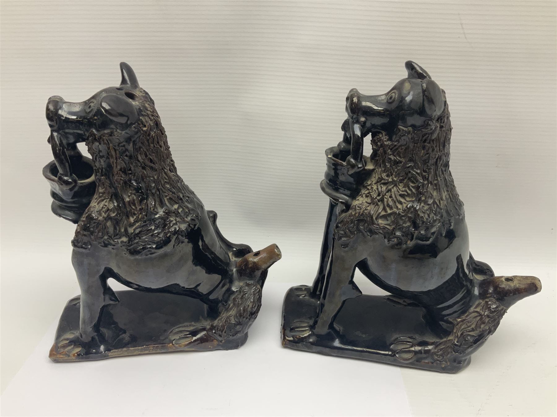 Pair of unusual early English pottery figures, modelled in the form of seated dogs with baskets between their jaws, the tails forming whistles, each upon rectangular base, overall H22cm