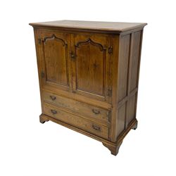 Oak drinks or media cabinet, projecting moulded cornice over two Gothic arch panelled doors on sliding tracks enclosing open storage, two drawers with brass drop handles, on bracket supports