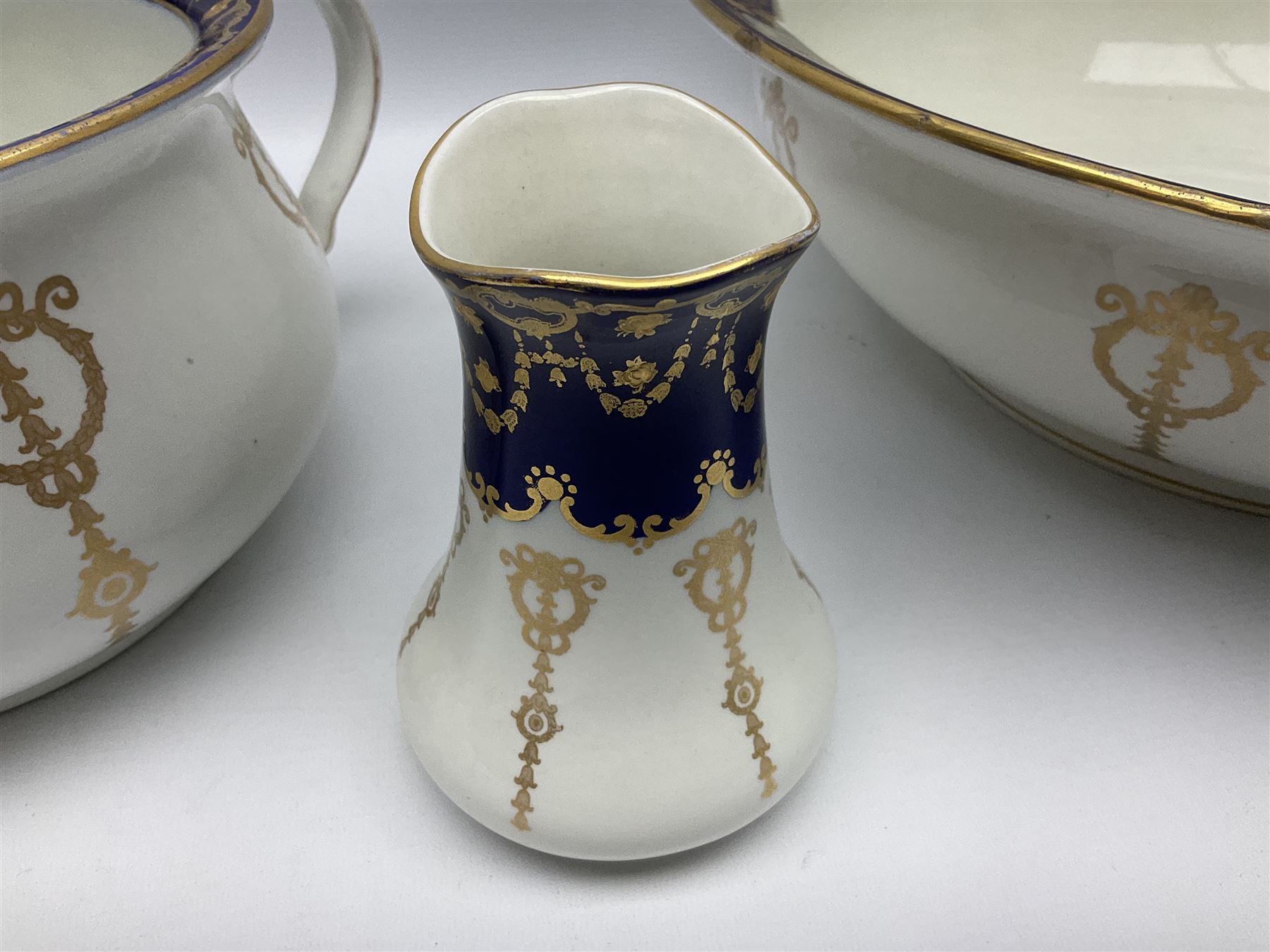 Early 20th century Bishop and Stonier four piece toilet set, comprising washbowl, wash jug, toothbrush pot, and chamber pot, each  decorated with deep blue band and husk swags and festoons in gilt, with printed Caduceus Bisto marks beneath and printed retailers mark 'Manufactured for Harrods Limited London', wash bowl D43cm, wash jug H31.5cm