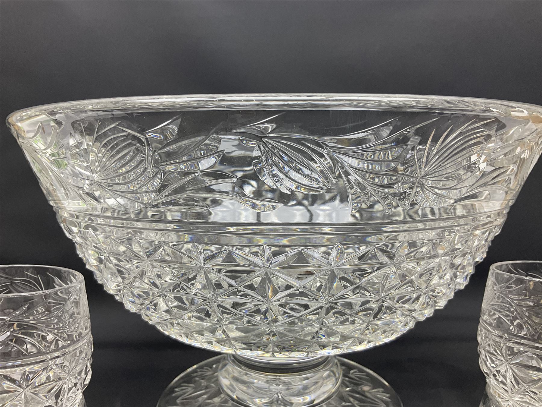 Large Stuart crystal pedestal punch bowl, of circular form, the rim with engraved floral decoration, upon spreading circular foot with radial cut decoration, with seven matching Stuart crystal drinking glasses, each with a C handle, each acid signed beneath, bowl H20cm