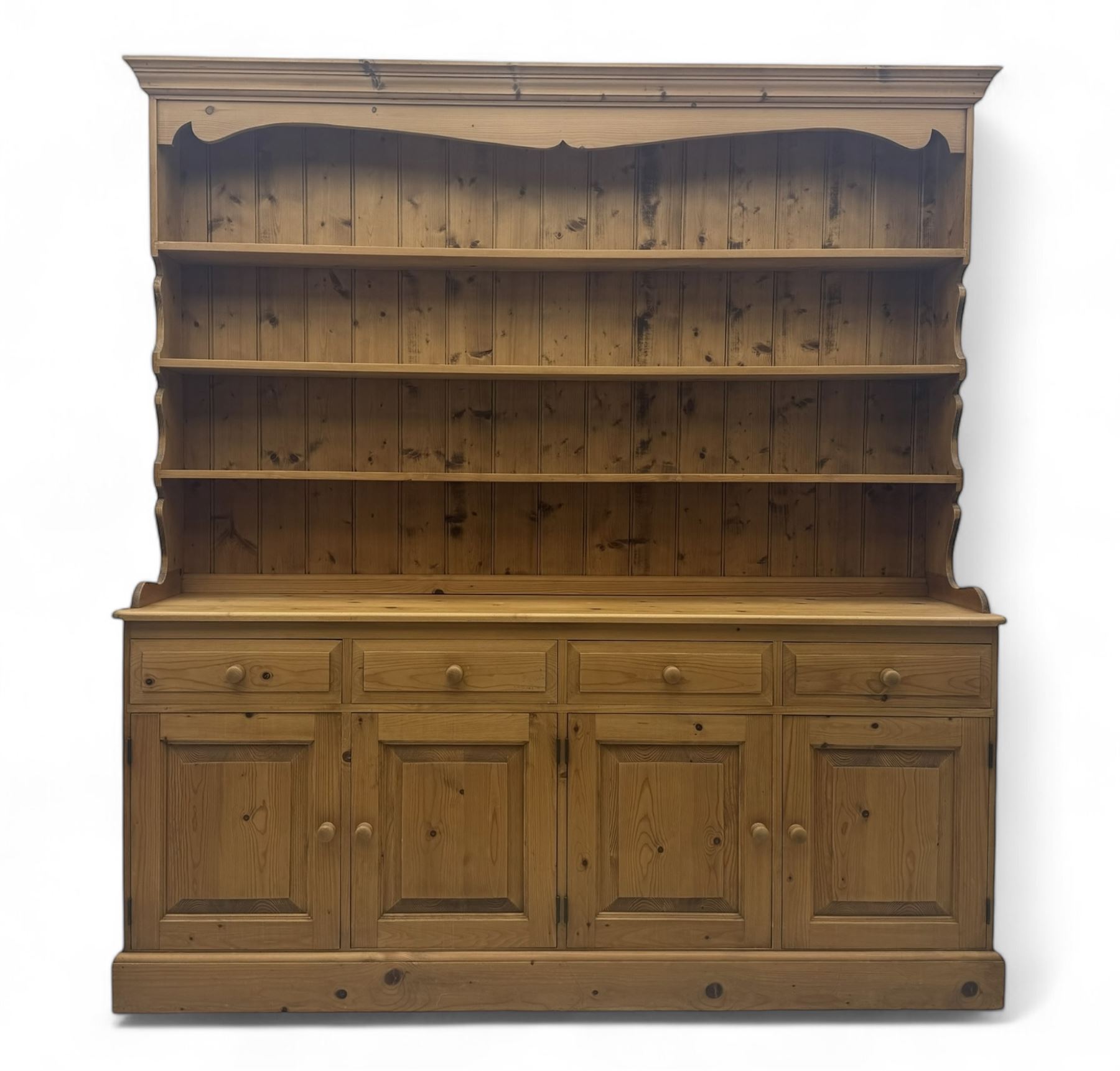 Large traditional pine dresser, shaped cornice over three open shelves, base fitted with four drawers above four panelled cupboards, each with turned wooden knobs, on plinth base