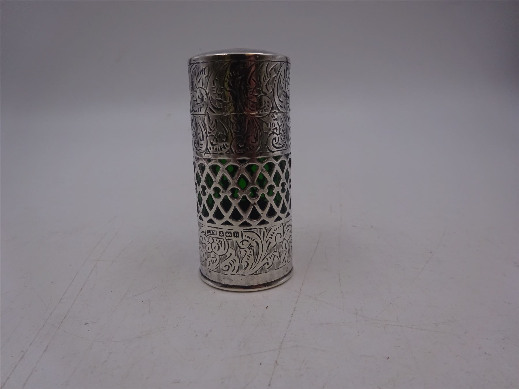 Early 20th century silver mounted green glass scent bottle, the silver body engraved profusely with foliate scrolls, with central pierced latte band revealing the green glass beneath, the hinged lid opening to reveal wooden stopper, hallmarked George Edwin Walton, Birmingham 1912, H7cm