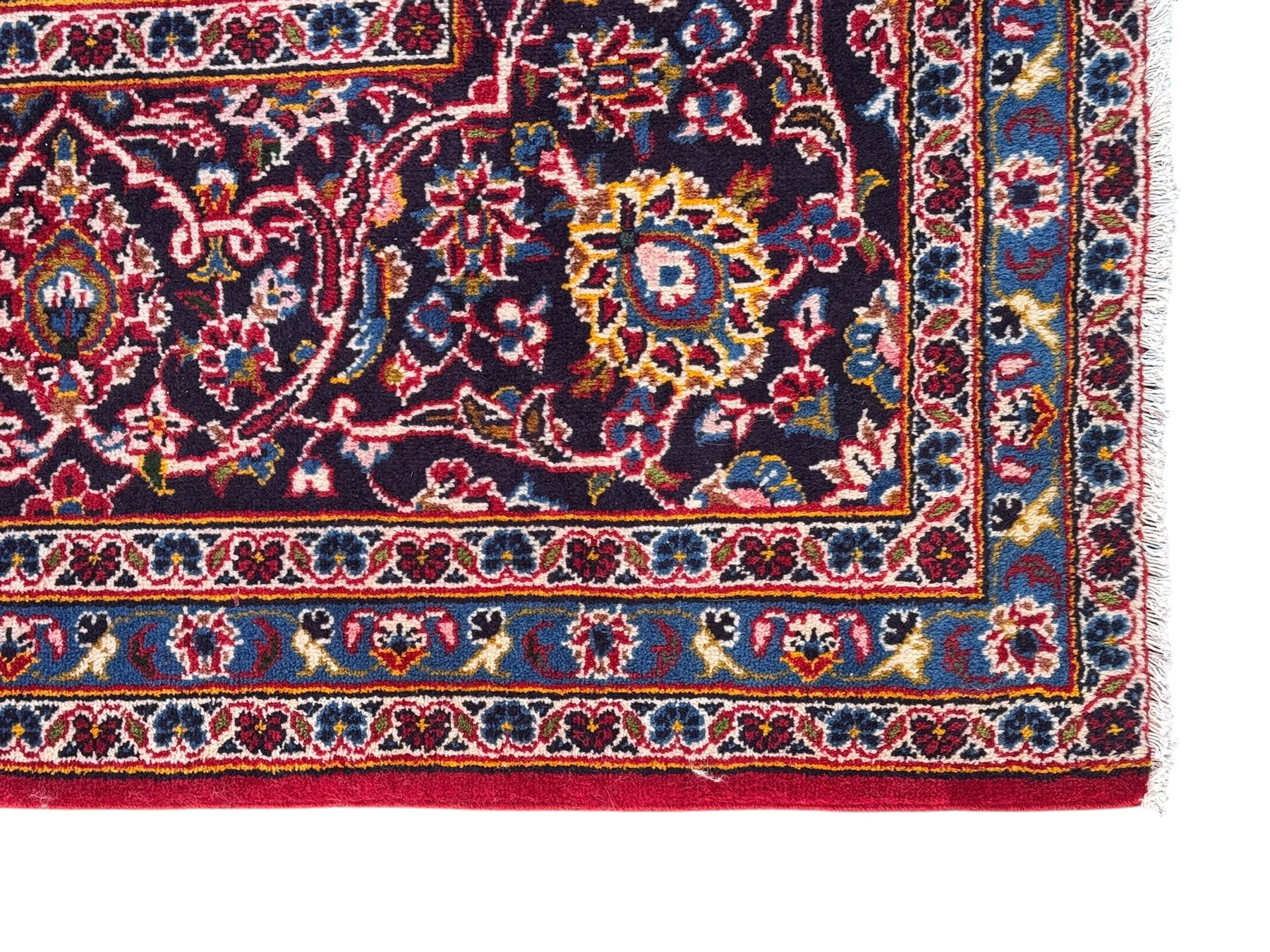 Large Kashan crimson ground carpet, central indigo medallion with stylised floral motifs, flanked by matching spandrels, bordered by multiple bands featuring repeating foliate and floral designs throughout