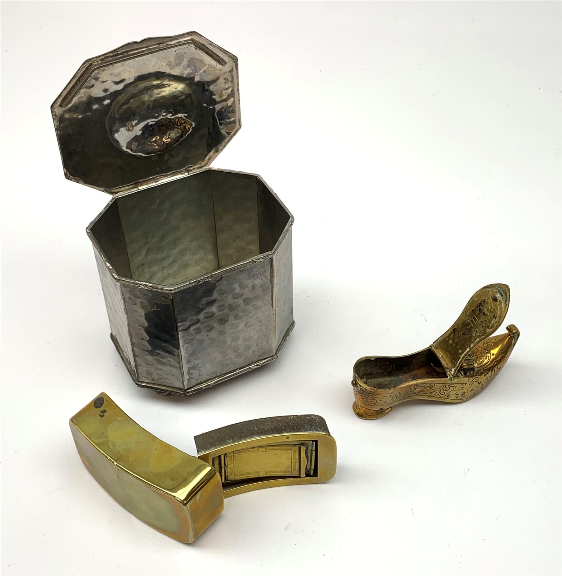 A 19th century brass three compartmented snuff box, of curved oblong form, L7.5cm, together with a later brass box in the form of a shoe, and an Arts and Crafts style Cobral Ware planished box, with canted corners and four bun feet, H10cm. (3). 