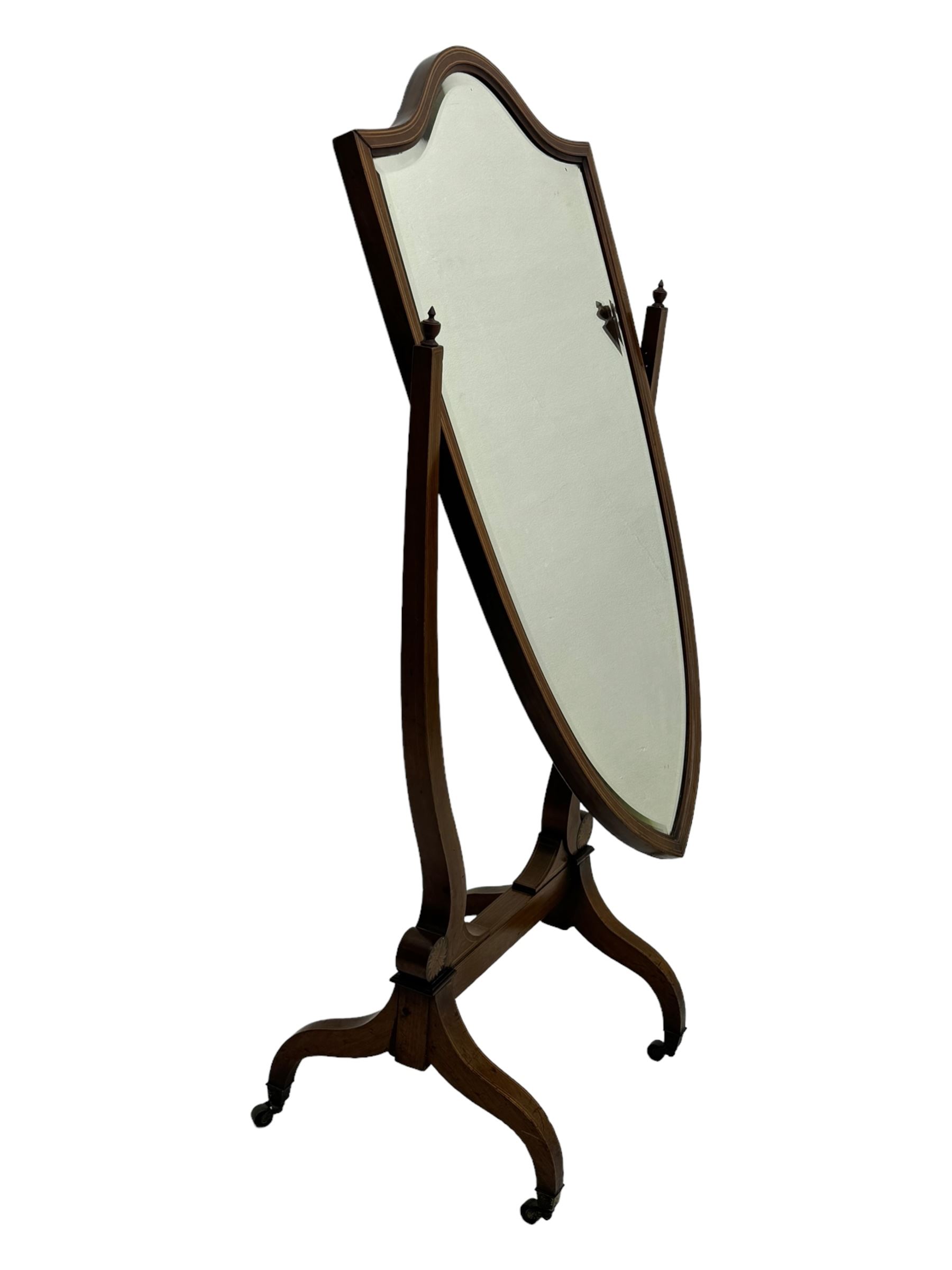 S. & H. Jewell - Edwardian mahogany cheval dressing mirror, shield shaped bevel edged mirror plate within an inlaid mahogany frame, supported by a pair of curved uprights topped with finials and terminating in a scroll design with floral inlay, the reverse bearing makers plaque, standing on four shaped supports fitted with brass castors