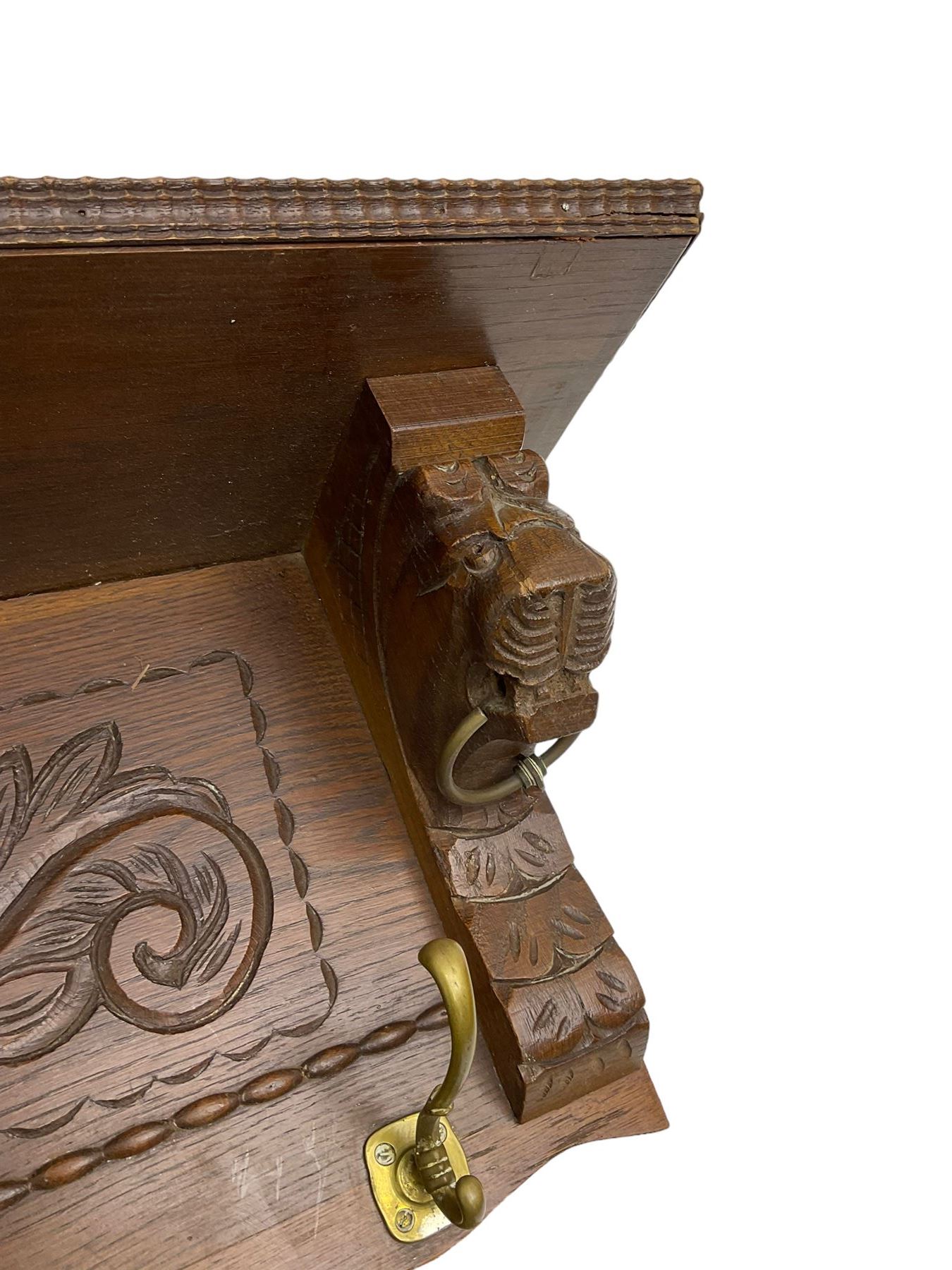 Late 20th century oak wall hanging coat rack, central bevelled oval mirror in foliate carved surround, decorated with S-scrolls and lion masks, fitted with needlework hanging 