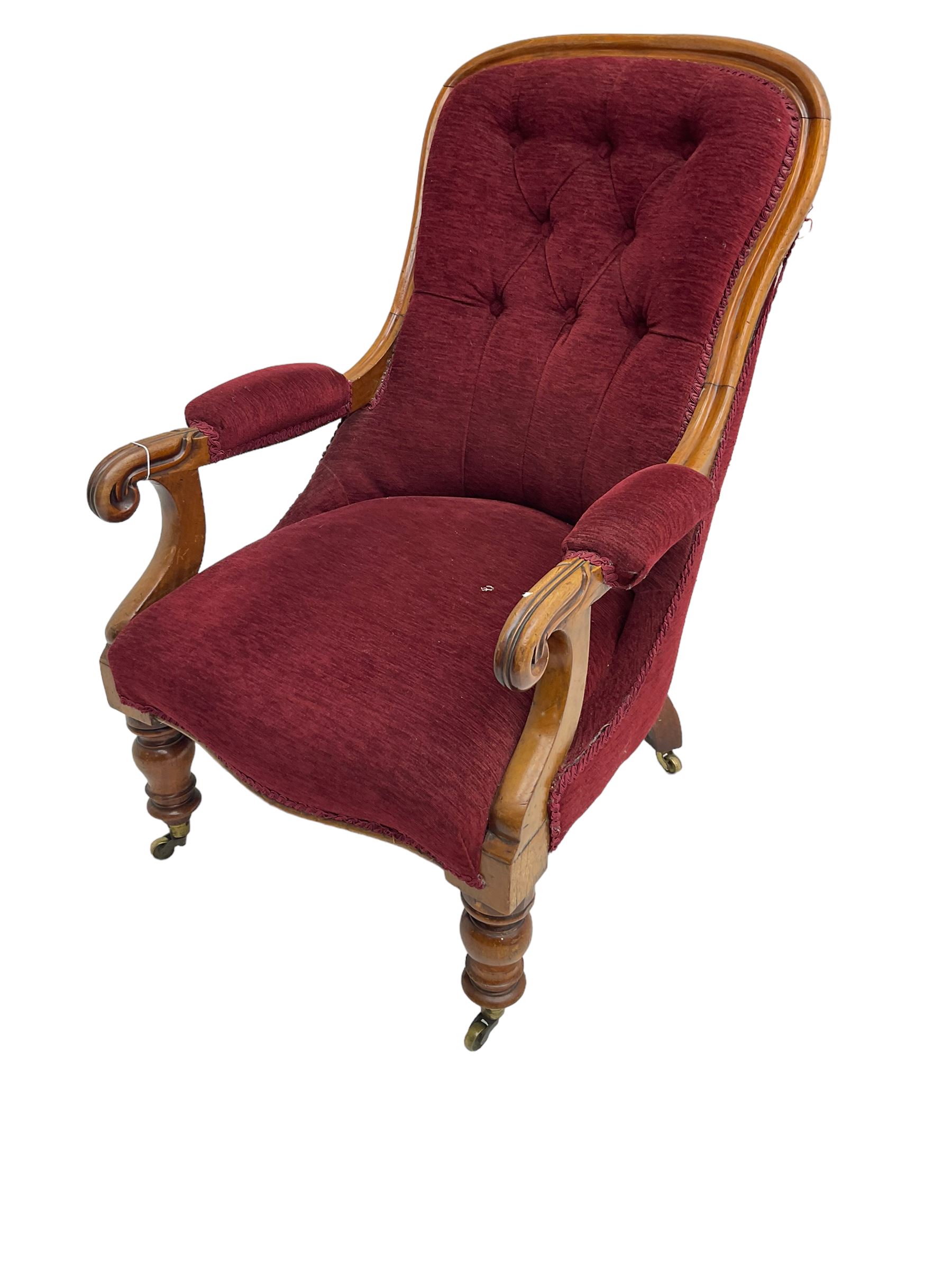 Victorian mahogany framed open armchair, upholstered in buttoned red fabric, the arm terminals carved with scrolls, on turned front supports with brass cups and castors