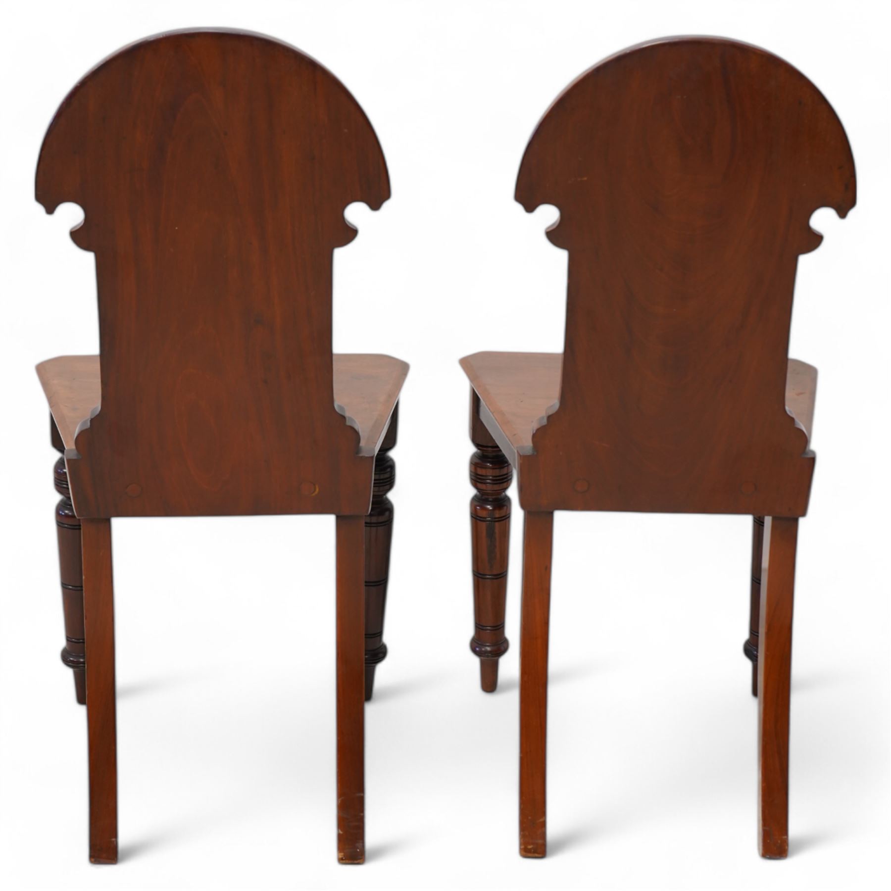 Pair of late Victorian mahogany hall chairs, arched cresting over foliate carved decoration and carved roundel back, chamfered seat over ring turned front supports 