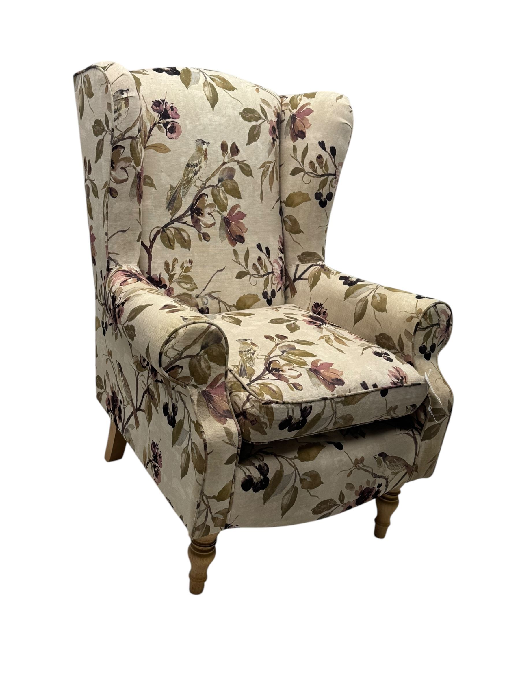 Hardwood-framed wingback armchair, upholstered in cream floral pattern fabric, on turned front feet