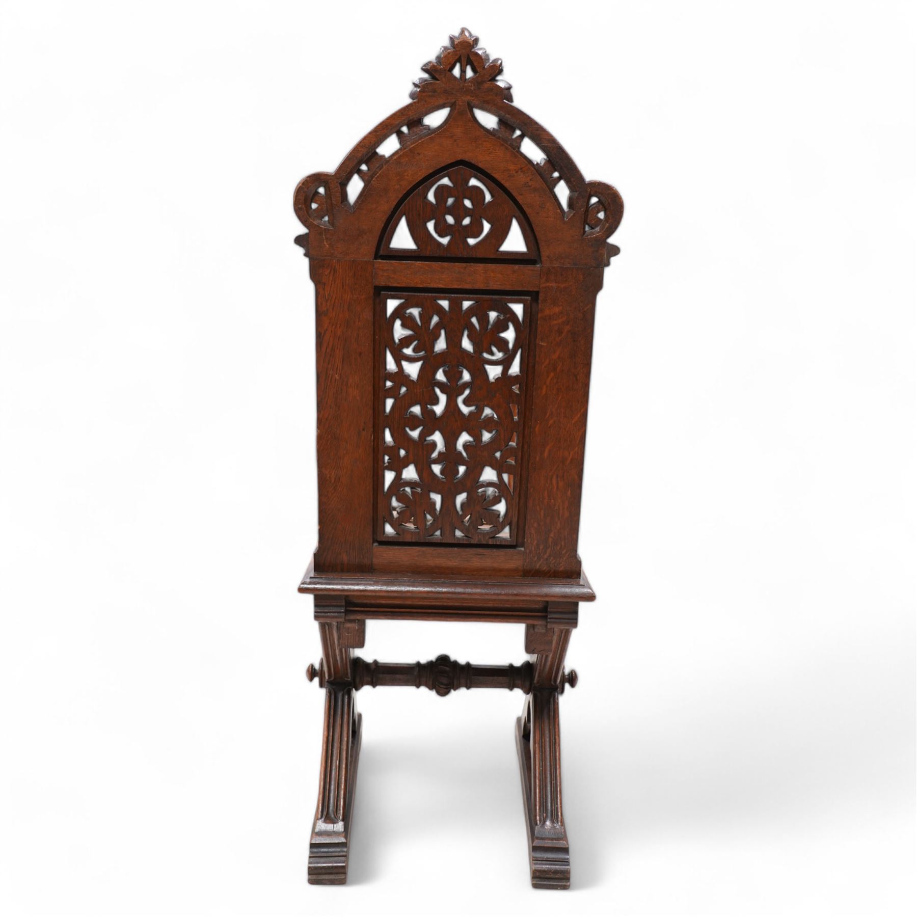 In the manner of Augustus Pugin - 19th century Gothic Revival carved oak hall chair, the pierced and carved arched pediment pierced and carved with scrolling foliage, the pierced back panel carved with a central pierced quatrefoil and leafage, panelled and eared seat over an architectural X-frame base with chamfered trefoil carvings and sledge feet