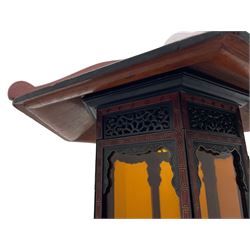 20th century Chinese black and red lacquered hardwood lantern stand, hexagonal shaped canopy top carved with flower heads and scrolls, the lantern fitted with amber tinted glass panes, pierced and carved upper panels, enclosed by two hinged doors, turned stem carved in relief with trailing vine leaves with fruits, stepped hexagonal base with carved decoration  