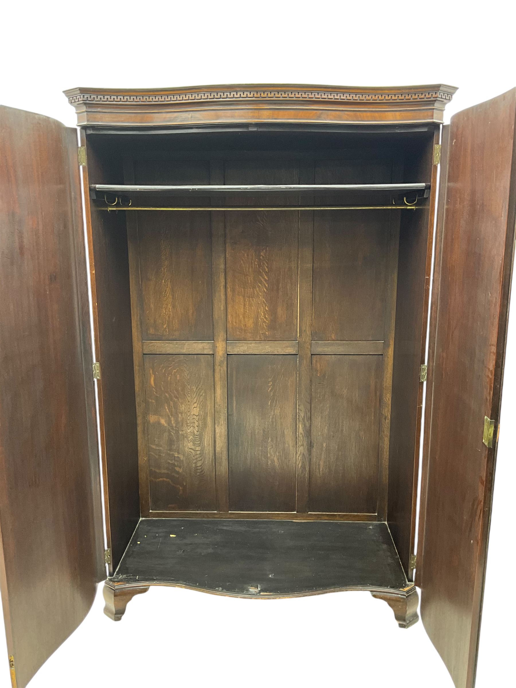 Early 20th century mahogany serpentine double wardrobe, moulded cornice over two figured doors, the interior fitted with hanging rail and shelf, canted and fluted uprights, on bracket feet 